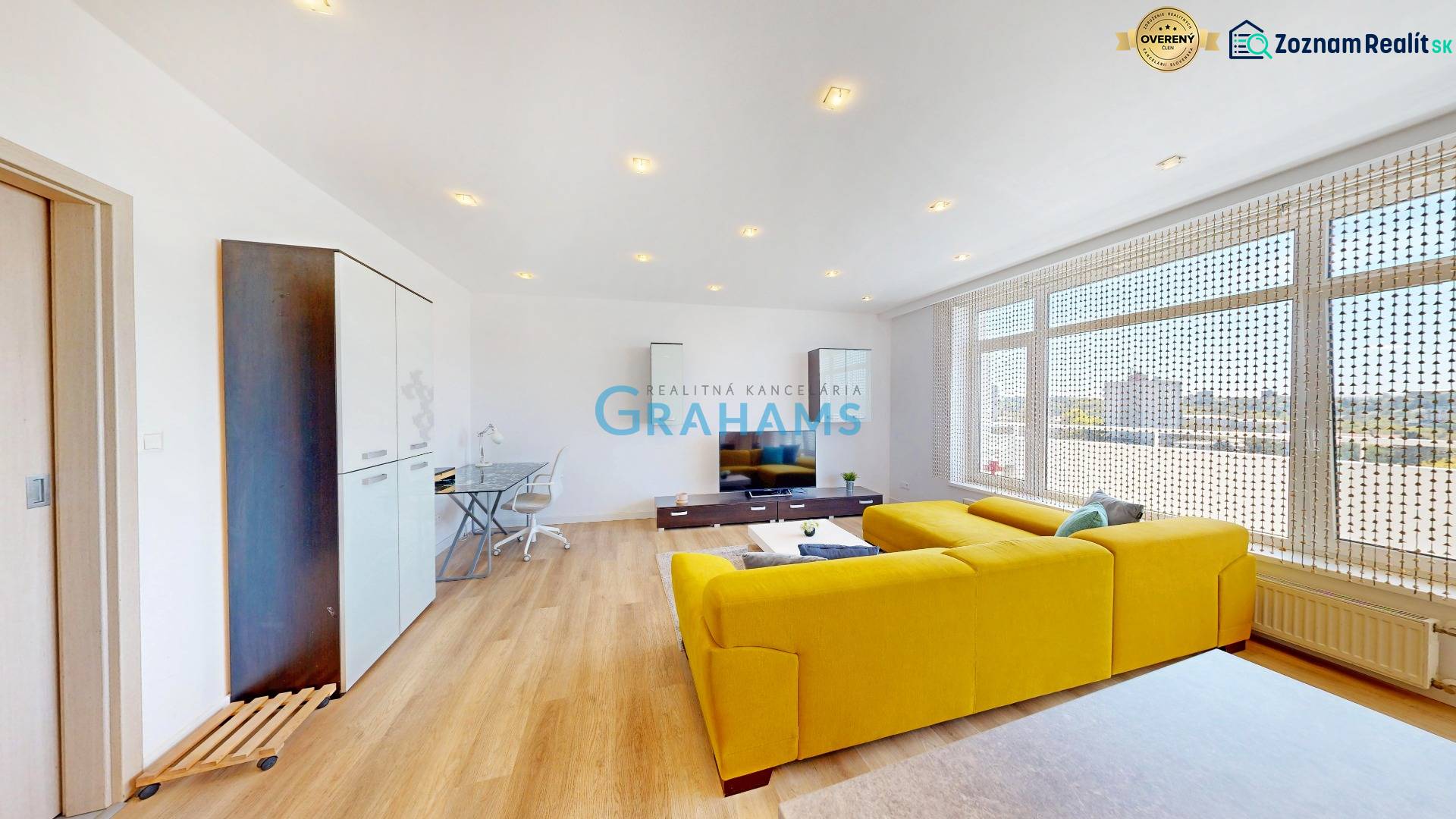 Living room in a two-room apartment with a wooden decor floor and a yellow sofa.