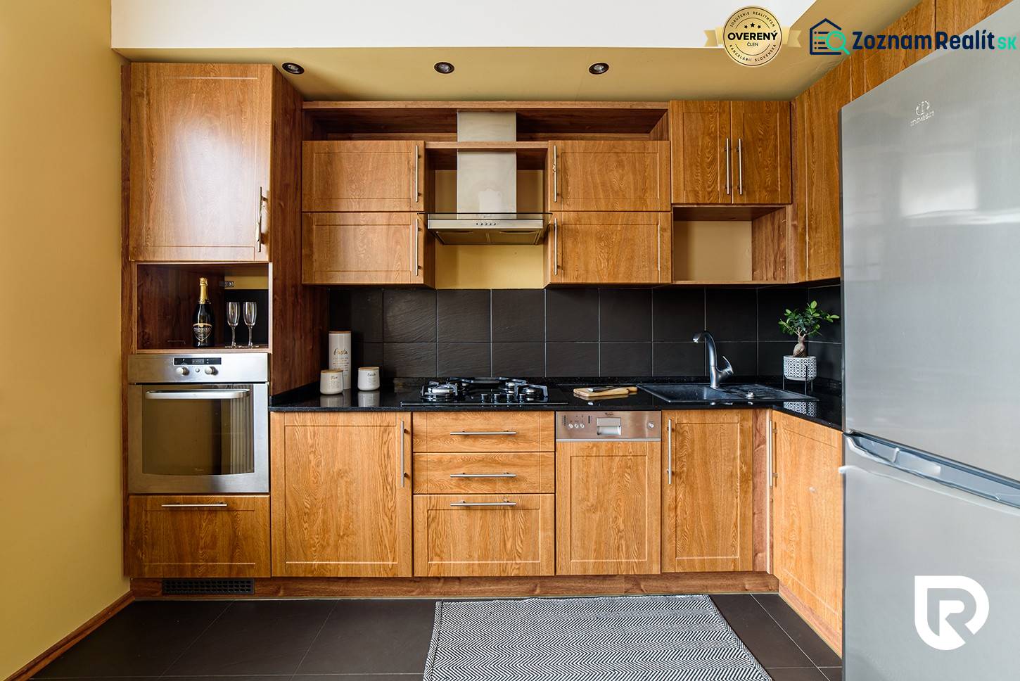 A kitchen in a 2-room apartment with wooden cabinets and a black countertop.