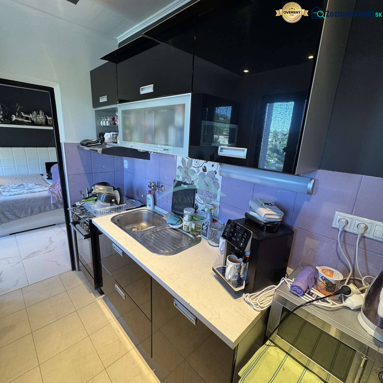 A kitchen in a 2-room apartment with black cabinets and purple tiles.