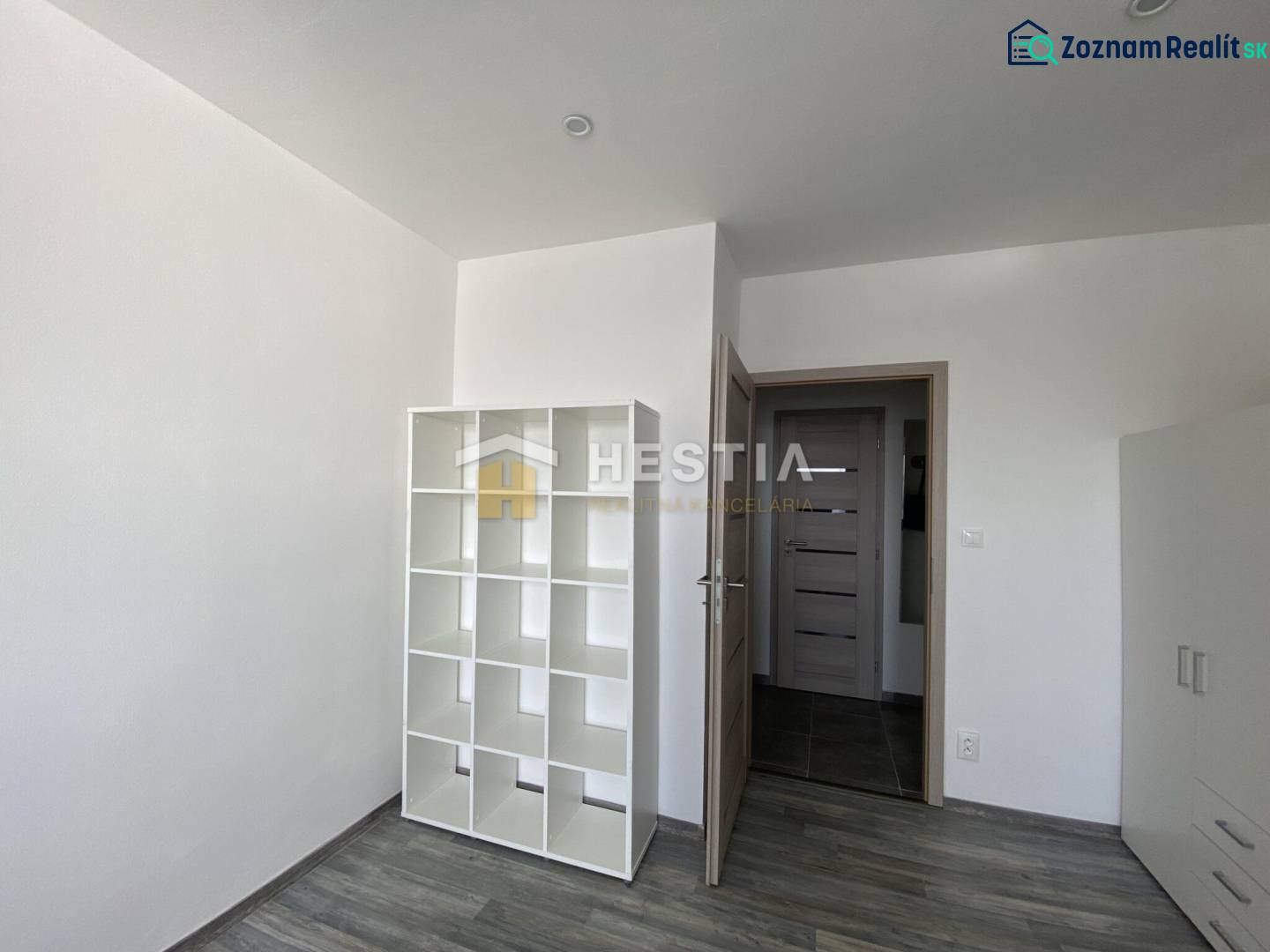 A room in a 2-room apartment with a shelving system and a floor with a wood decor.