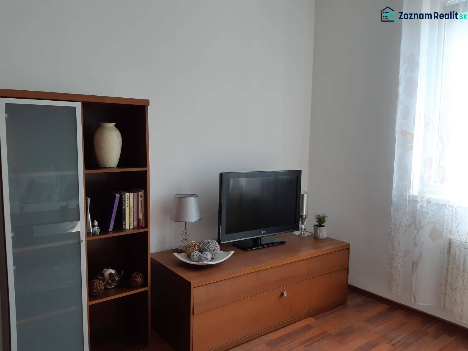 Living room with wood-patterned flooring, a bookshelf, a television, and decorative items.