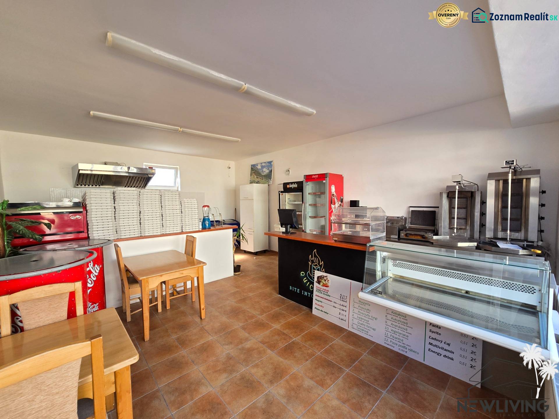 Interior of a gastro space with a counter, refrigerated display cases, and a stack of pizza boxes.