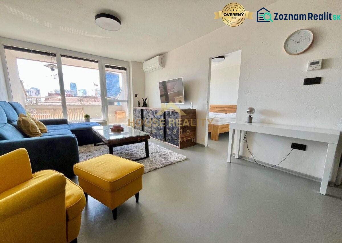 Living room of a three-room apartment with a sofa, television, and balcony.