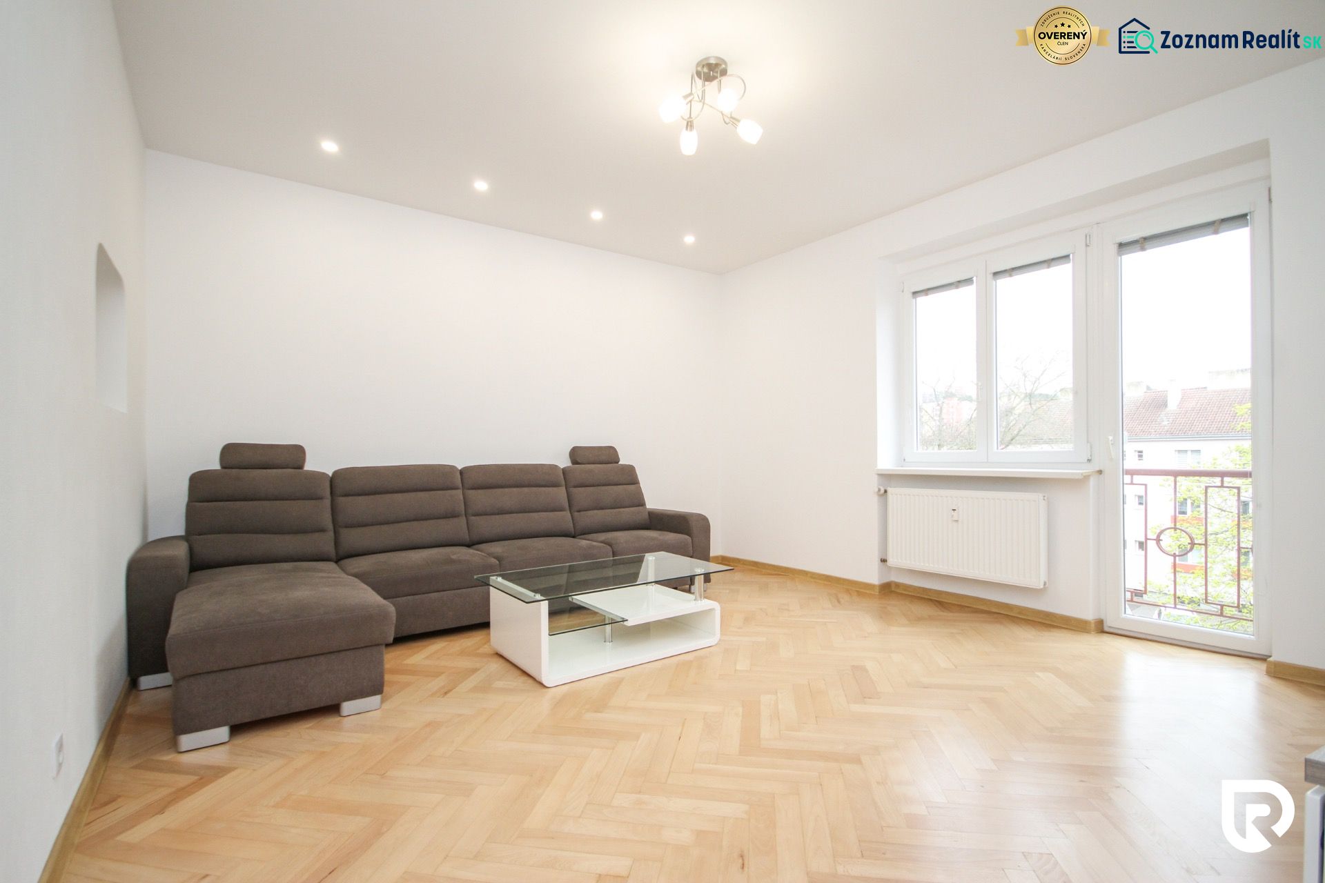 Living room in a two-room apartment with a sofa and wooden decor flooring.