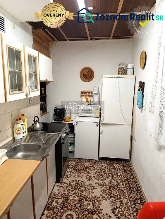 A kitchen in a cottage with simple furnishings, a carpet, and a white refrigerator.