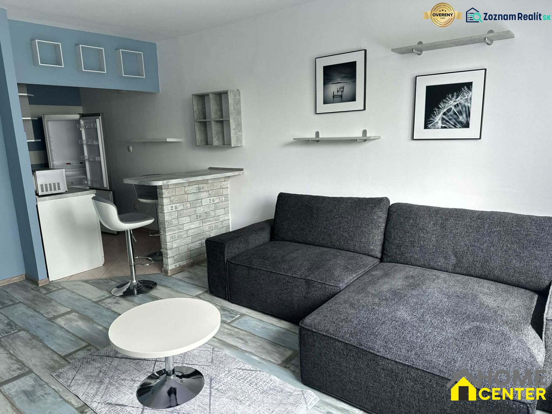 Two-room apartment with wood-patterned flooring, a sofa, and a bar counter.