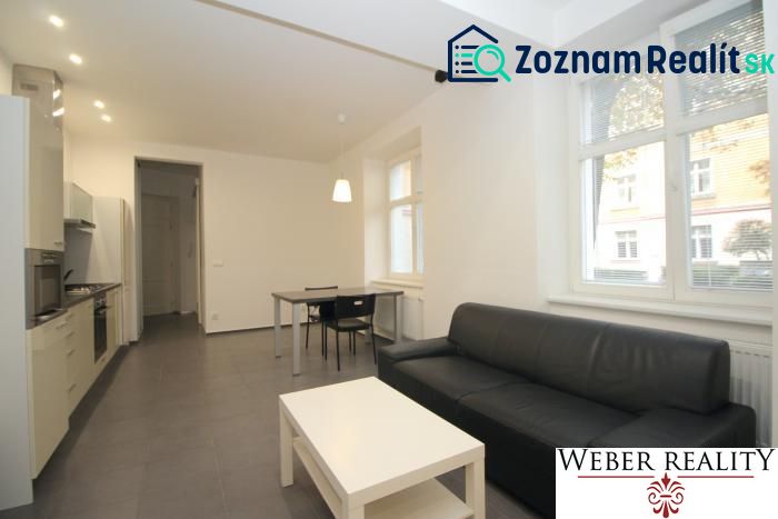 Living room in a two-room apartment with seating, kitchenette, and table on tiles.