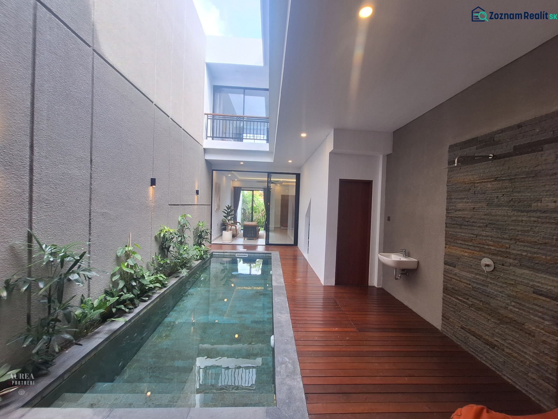 Villa with a pool, wooden decor flooring, plants, and a stone wall.