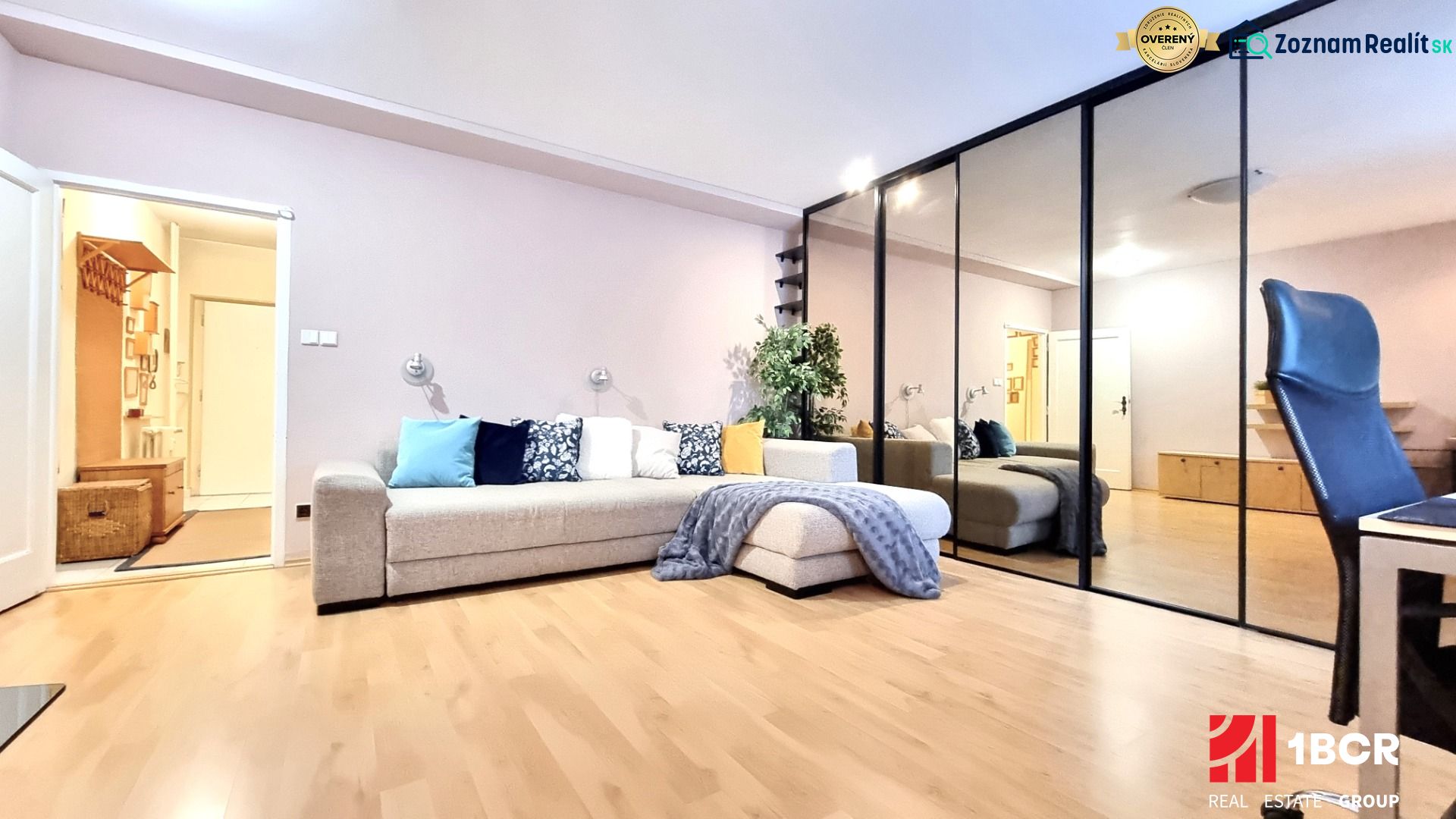 Living room with wood-patterned flooring, a sofa, mirrored built-in wardrobe, and lots of cushions.