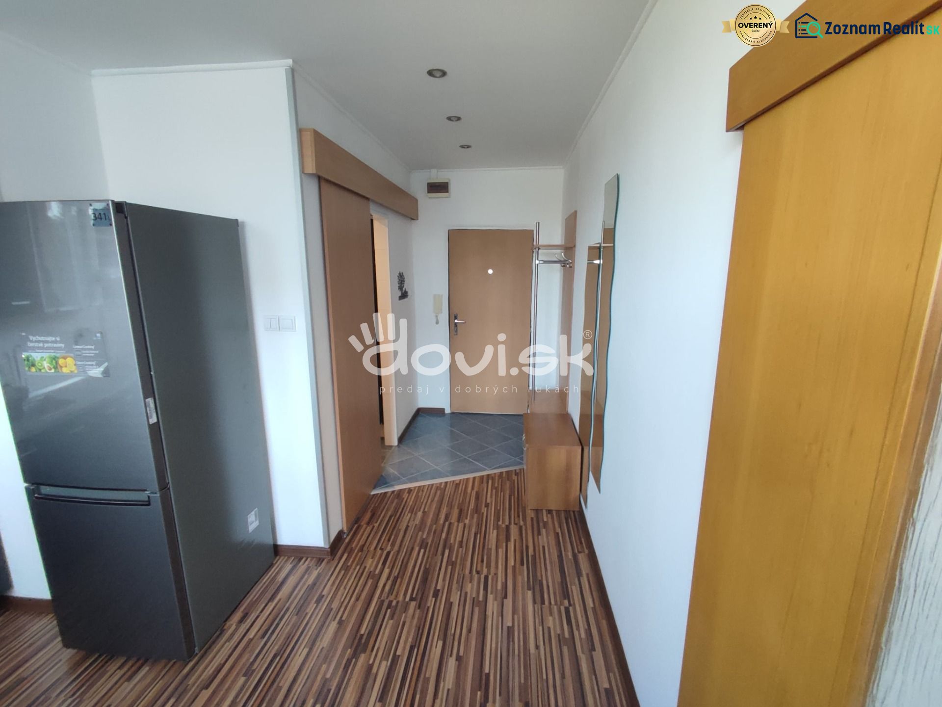 A narrow entrance space in a studio apartment with a wooden decor floor and a refrigerator.