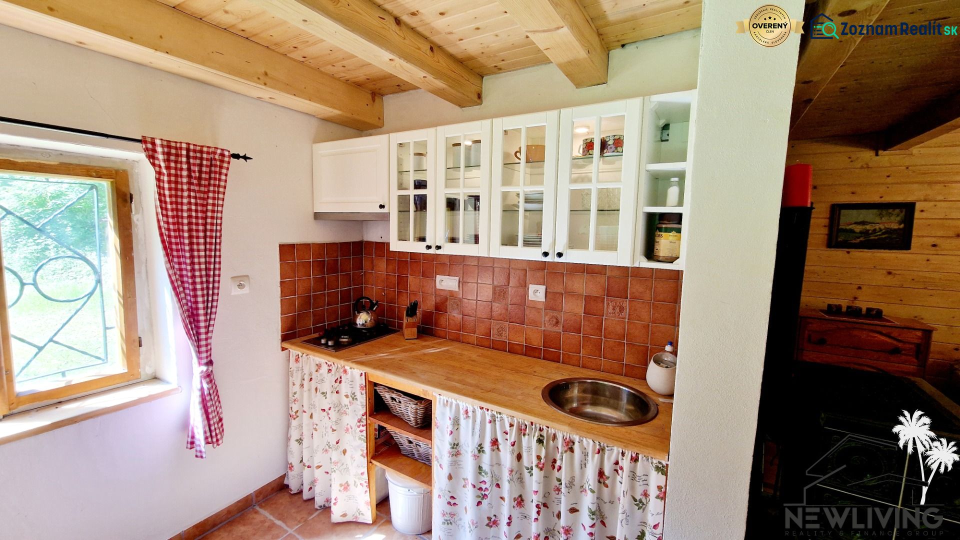 A kitchen in a cottage with white cabinets, ceramic tiles, and a wooden ceiling.