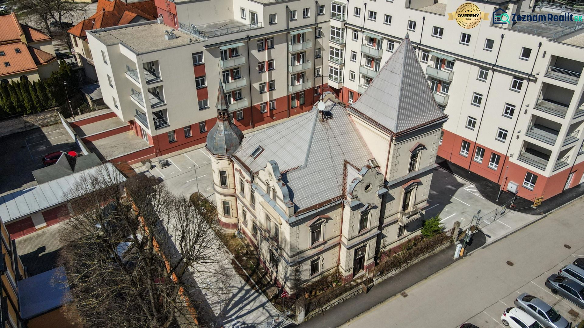 A historical building surrounded by modern apartment buildings on Hviezdoslavova Street in Trenčianske Teplice.