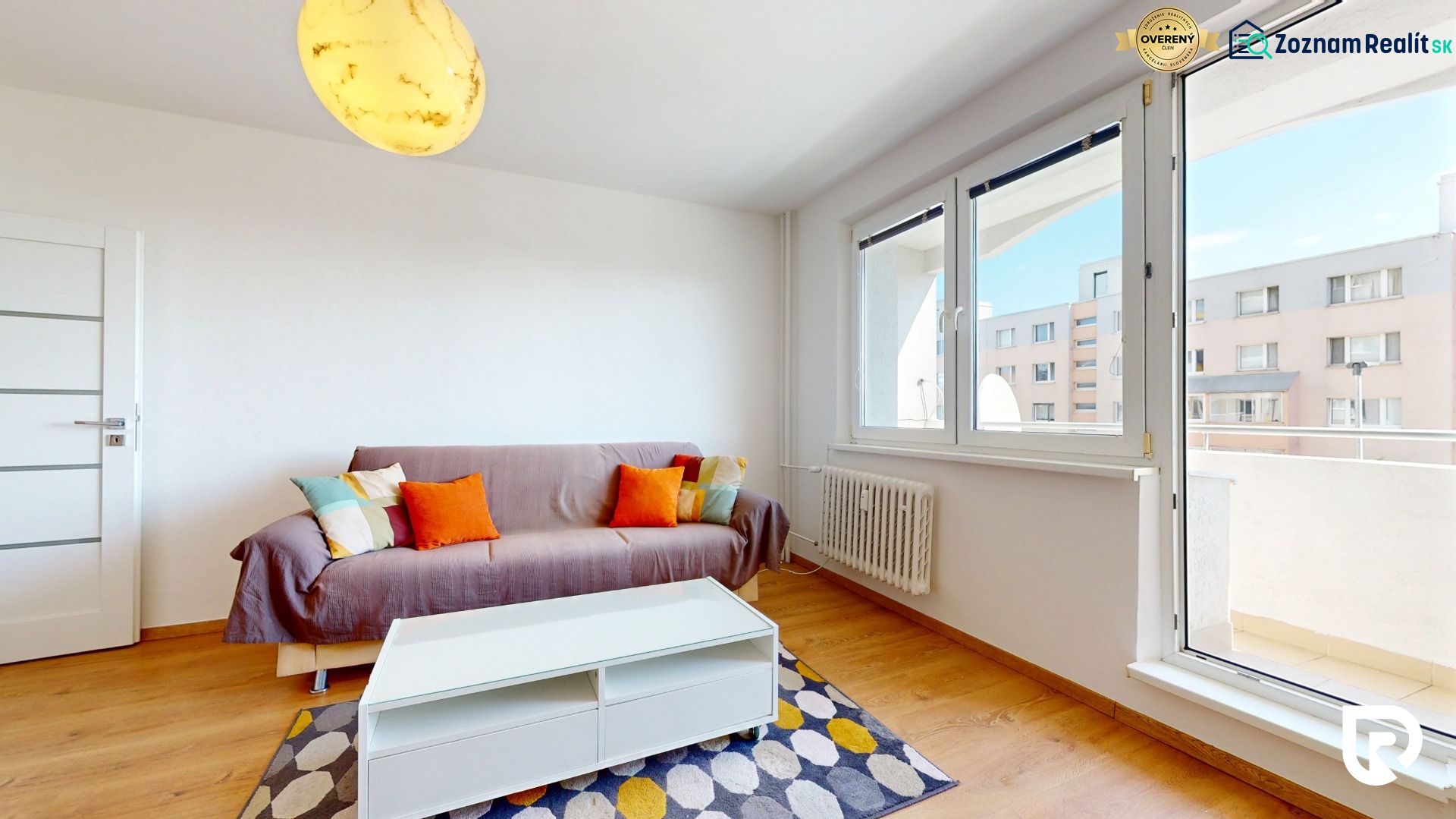 Living room in a two-room apartment with a wooden-patterned floor and colorful cushions on the sofa.