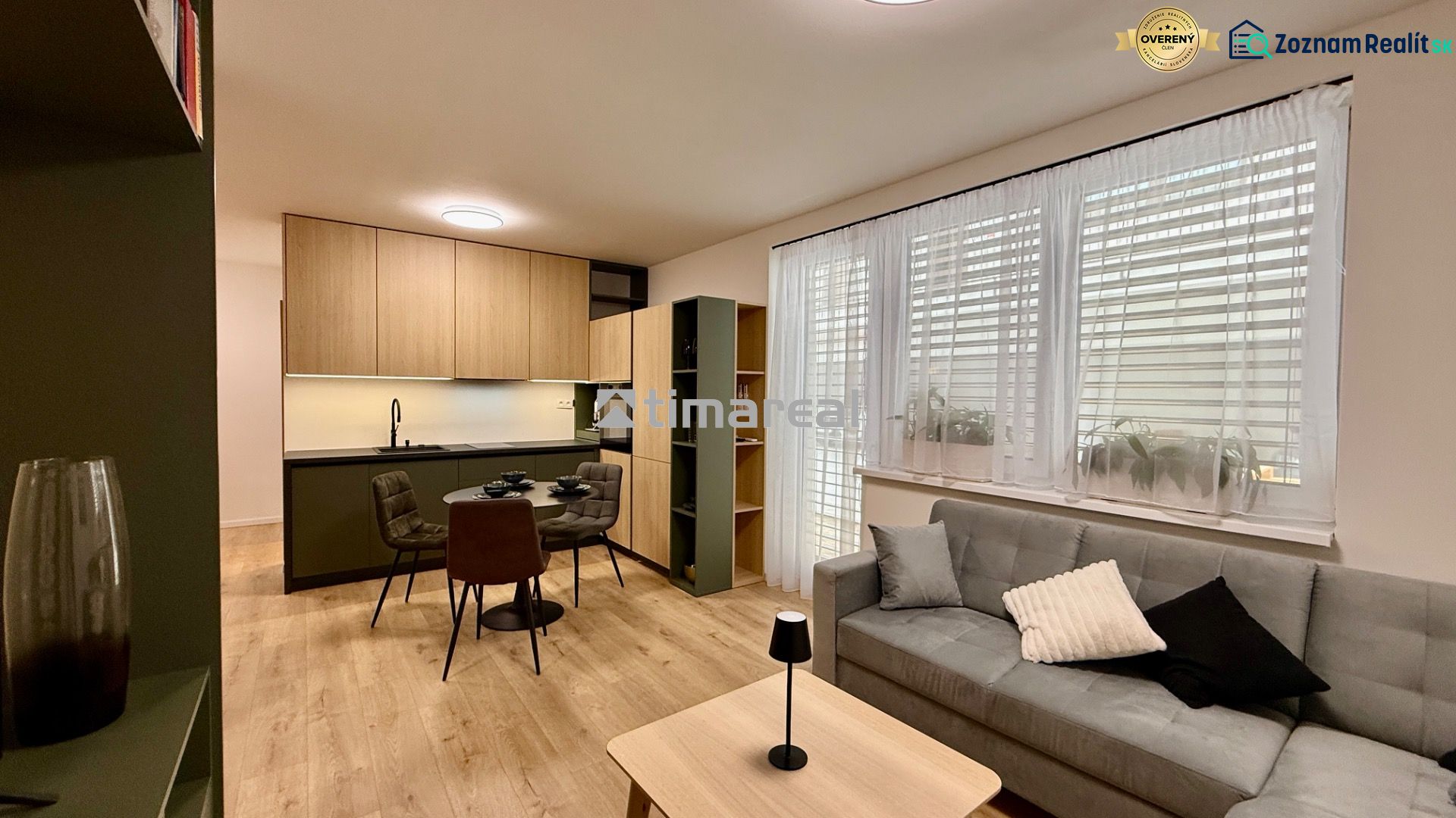 Living room with a kitchenette, dining table, and wooden decor flooring in a two-room apartment.
