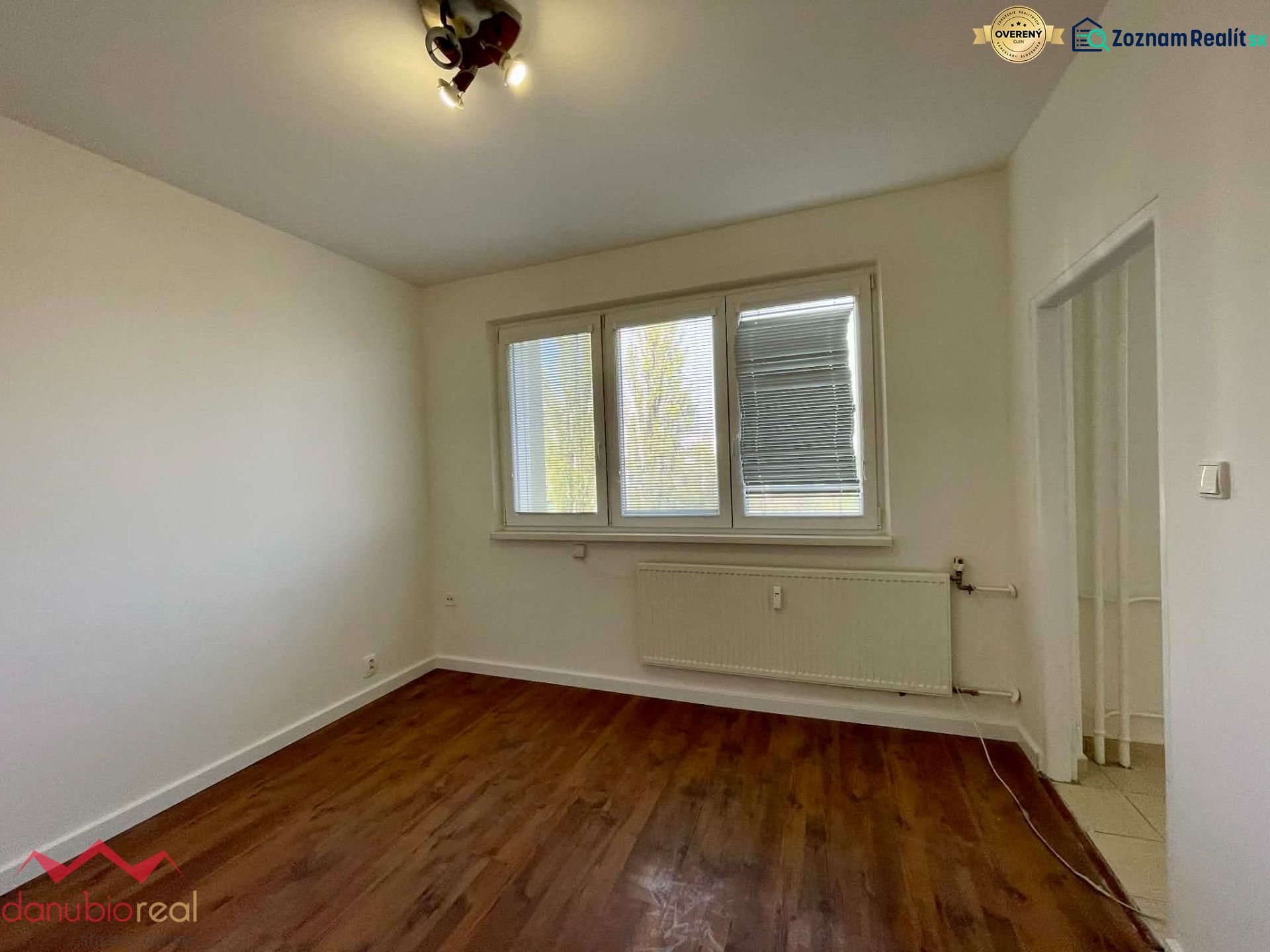 A room with a wooden decor floor in a one-room apartment, light walls, and a radiator.
