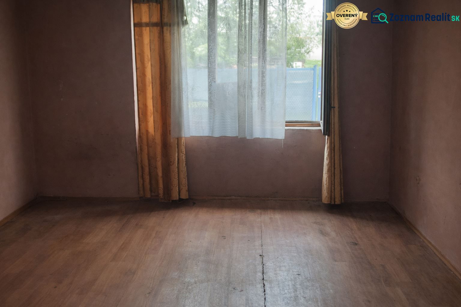 A room with a wooden floor design, curtains, and a window in a family house.