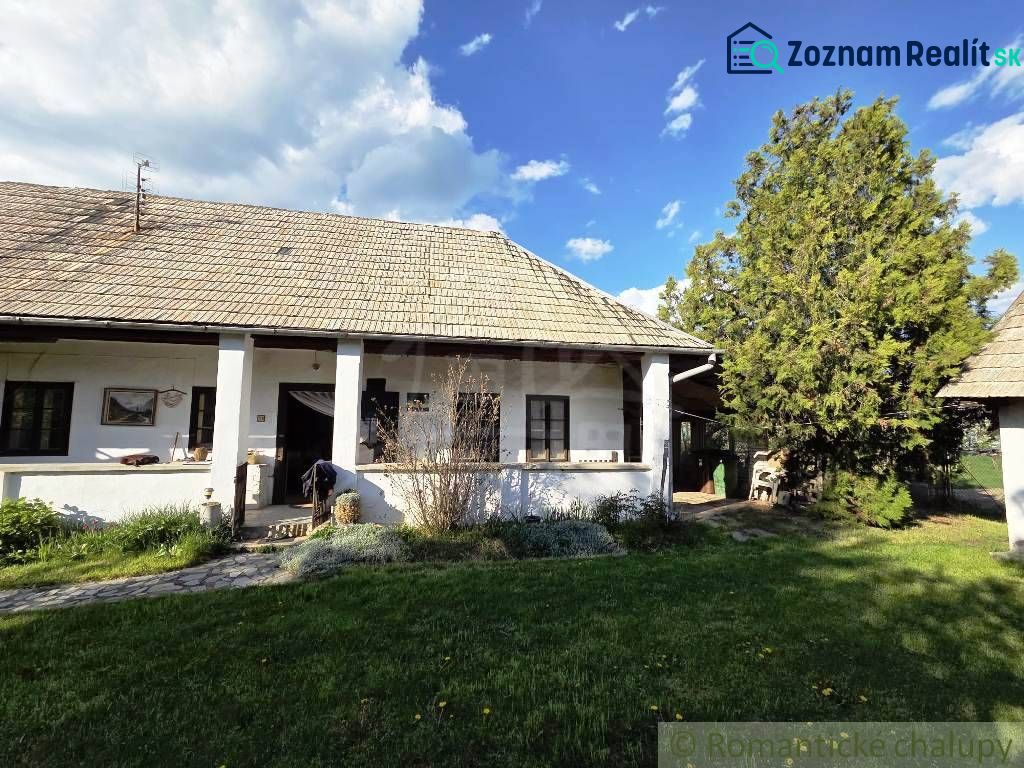 A cottage in Šahy with white walls and a traditional roof surrounded by greenery.