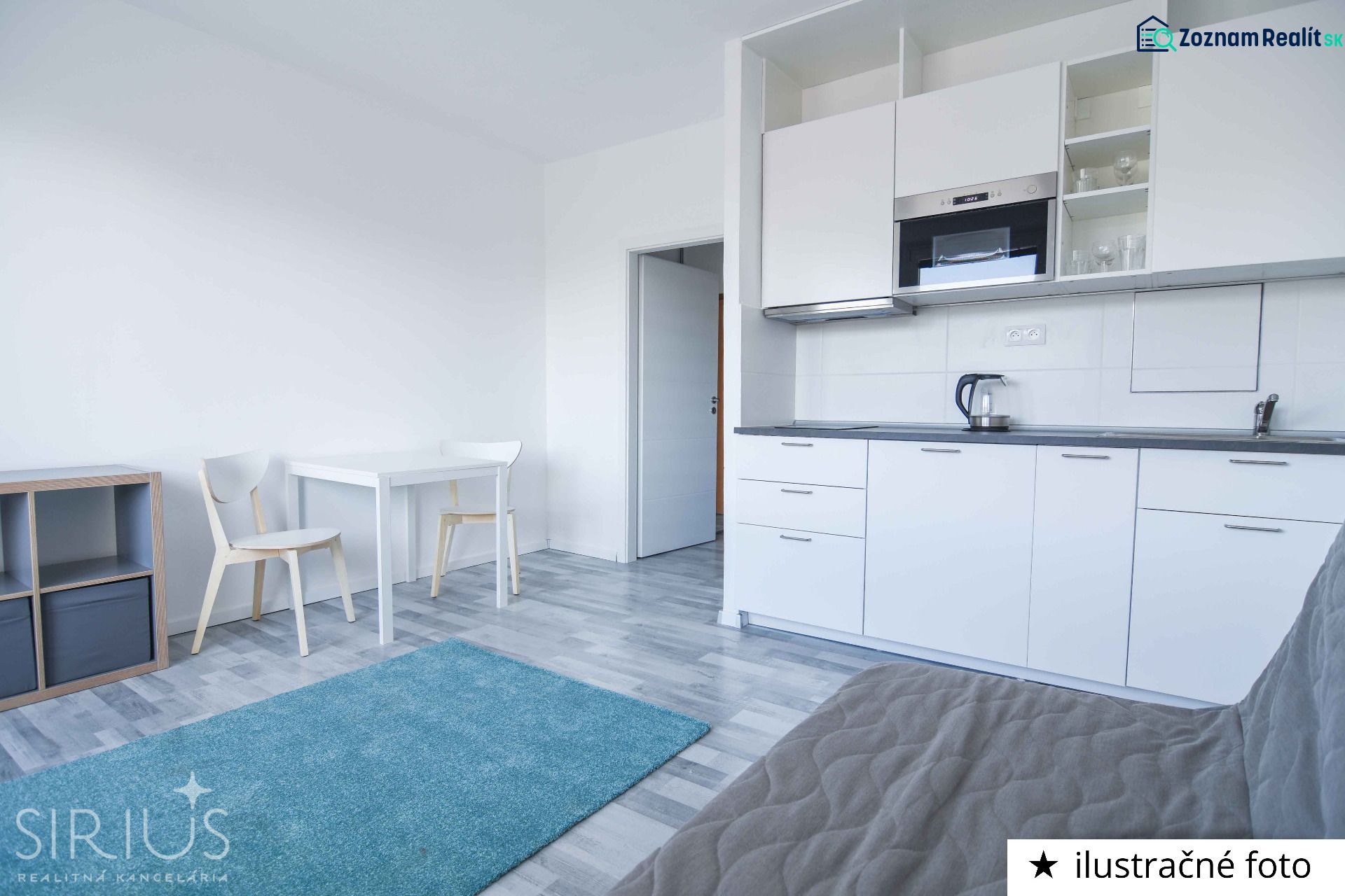 A studio apartment with a minimalist kitchen, dining table, and wooden decor flooring.