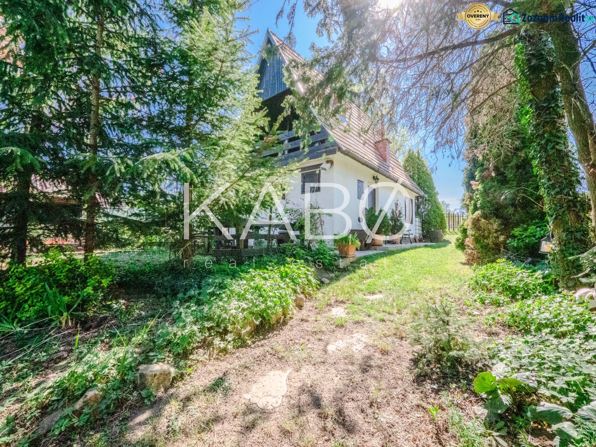 A cottage in Nitra surrounded by trees and a green lawn under a clear blue sky.