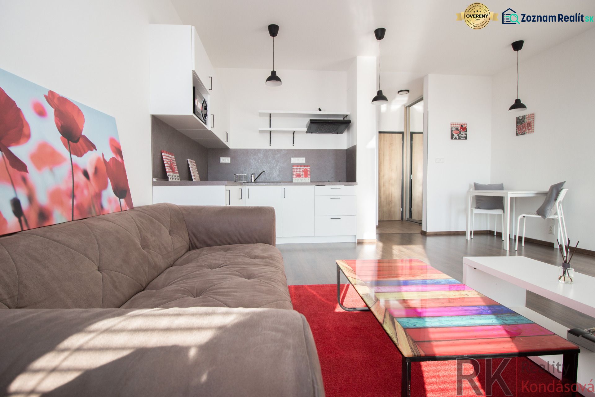 Living room with a sofa, kitchenette, and table in a studio apartment.