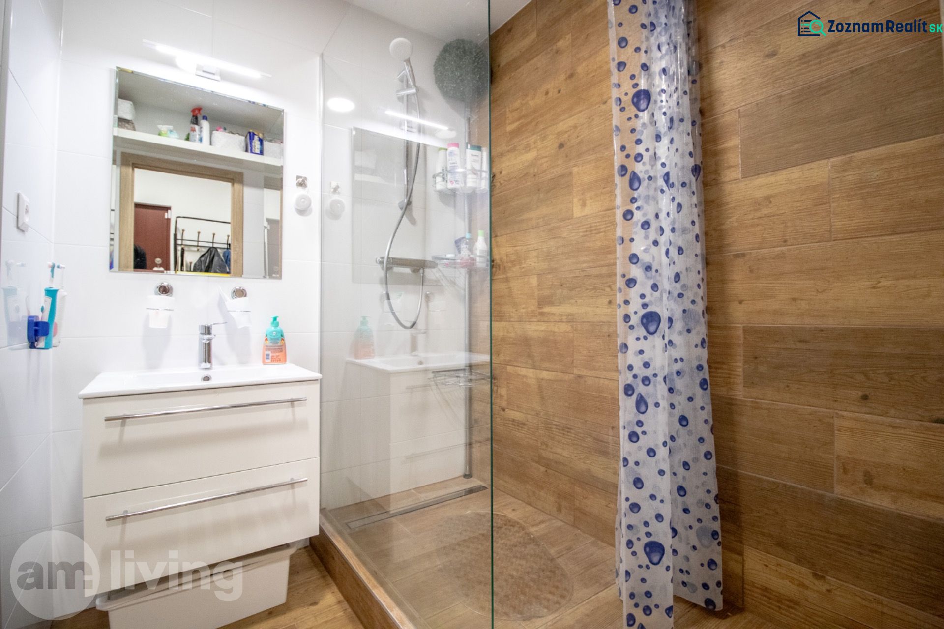 A bathroom in a 2-room apartment with a wooden decor floor, a shower corner, and a sink.