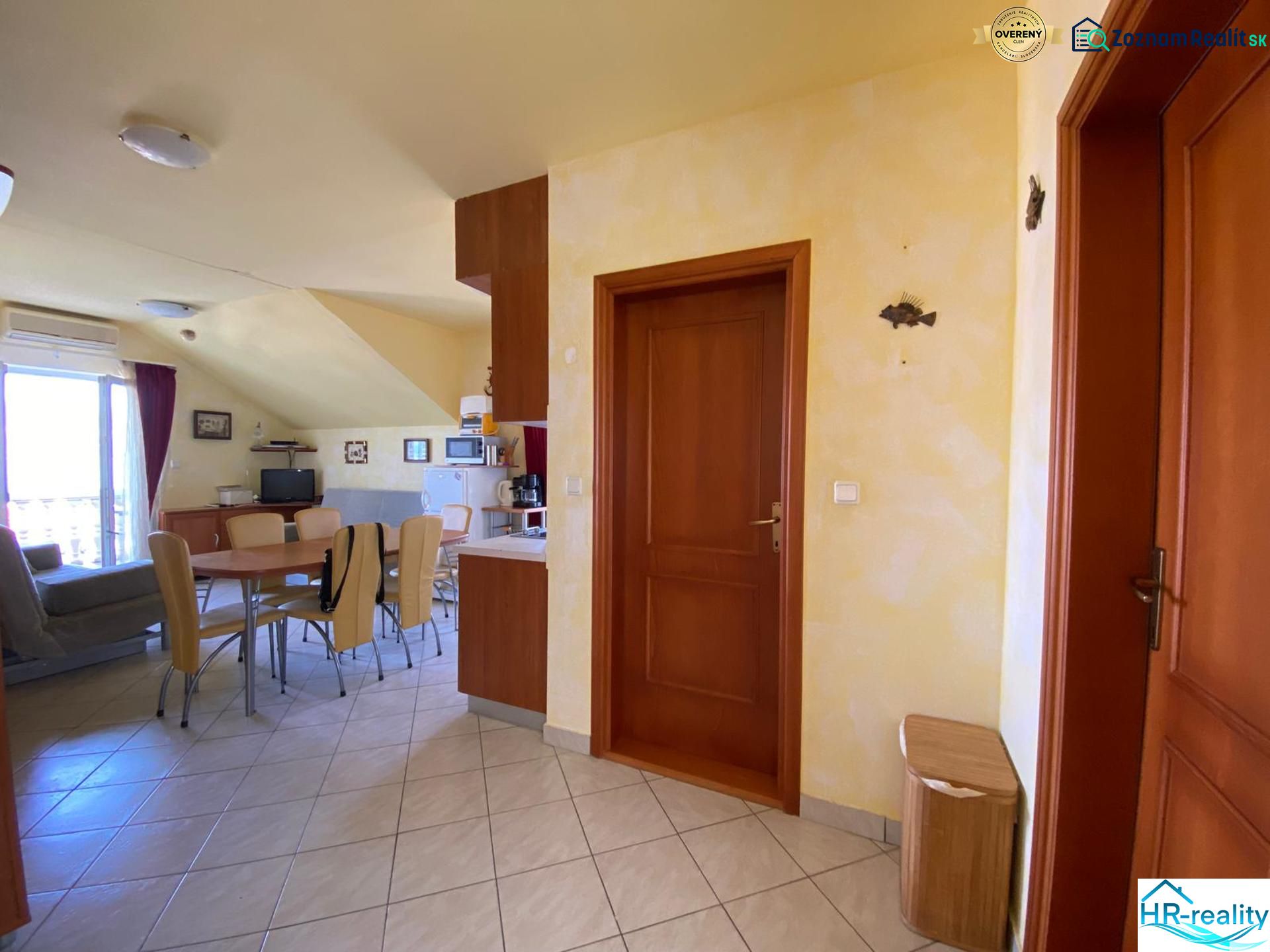 Interior of a holiday apartment with a dining table, kitchenette, and balcony doors.