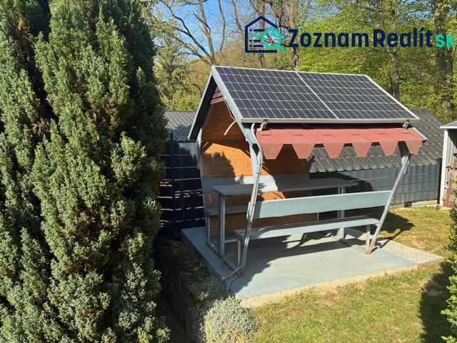 A cottage in Ilava with a gazebo and a solar panel in a garden surrounded by trees.