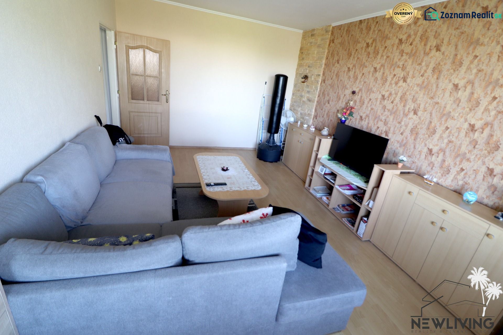 Living room in a two-room apartment with a gray sofa, television, and wooden decor flooring.