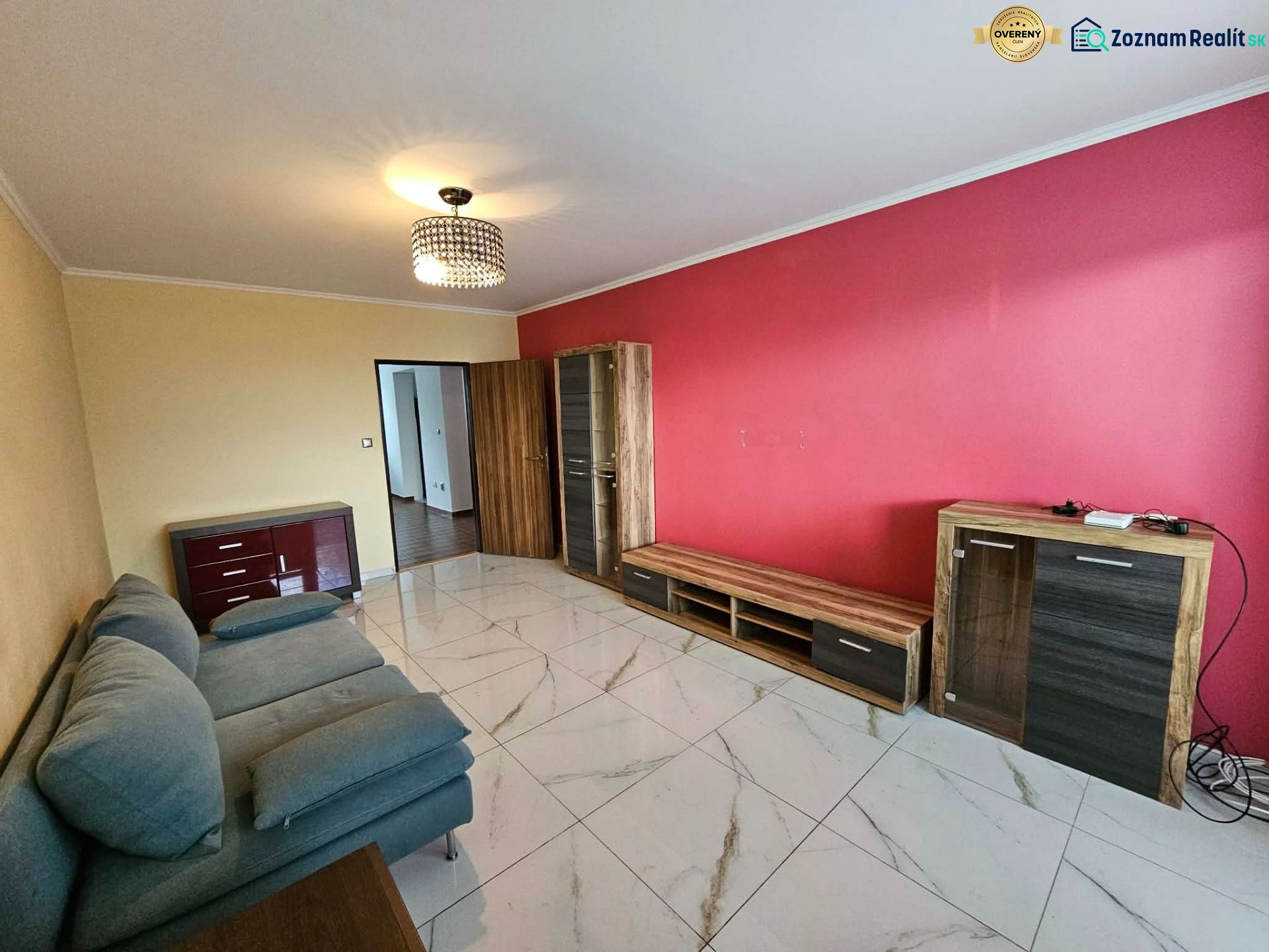 Living room in a three-room apartment with a striking red wall and a sofa.