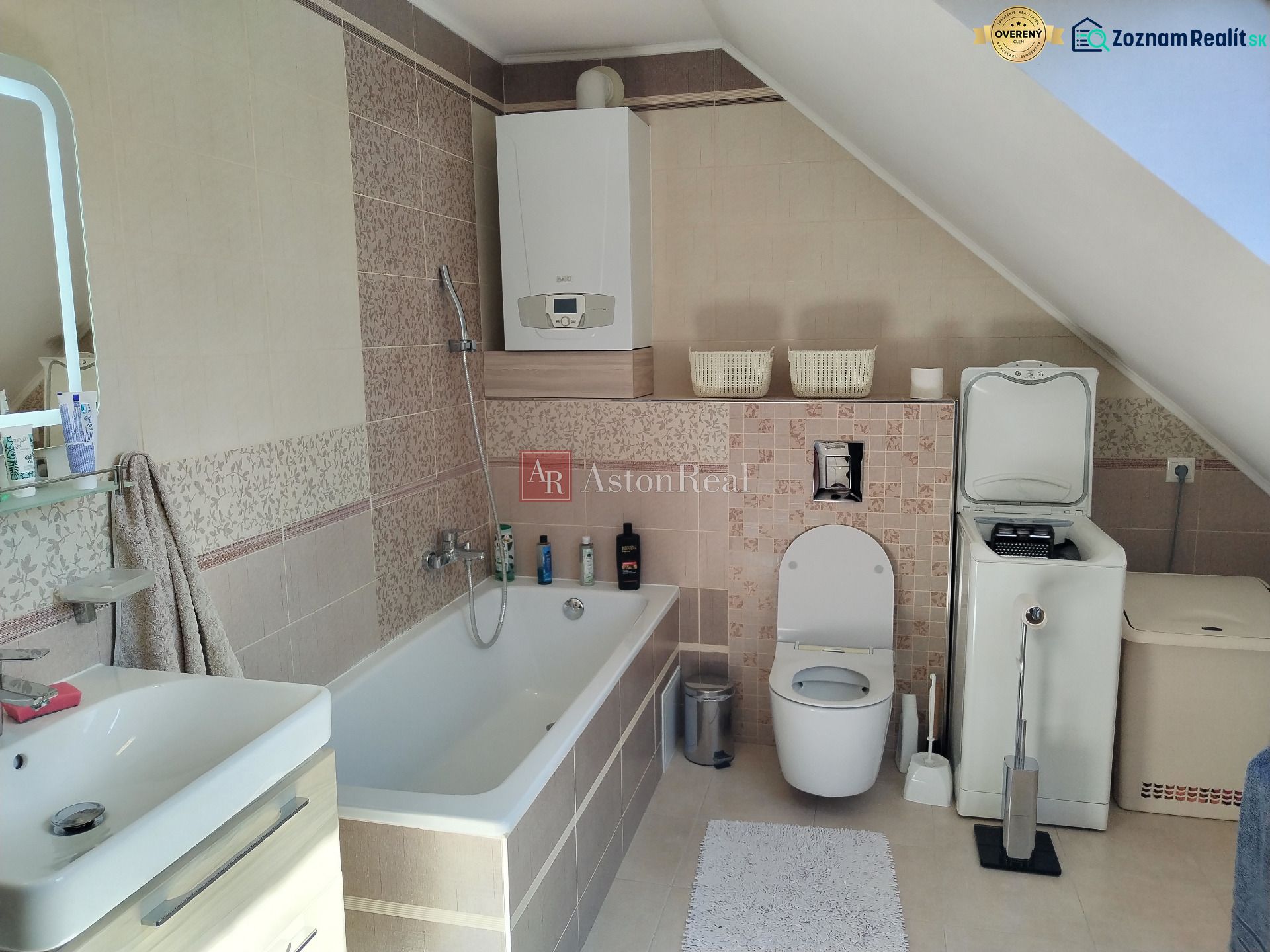A bathroom in a family house with a bathtub, toilet, and washing machine under a sloping roof.