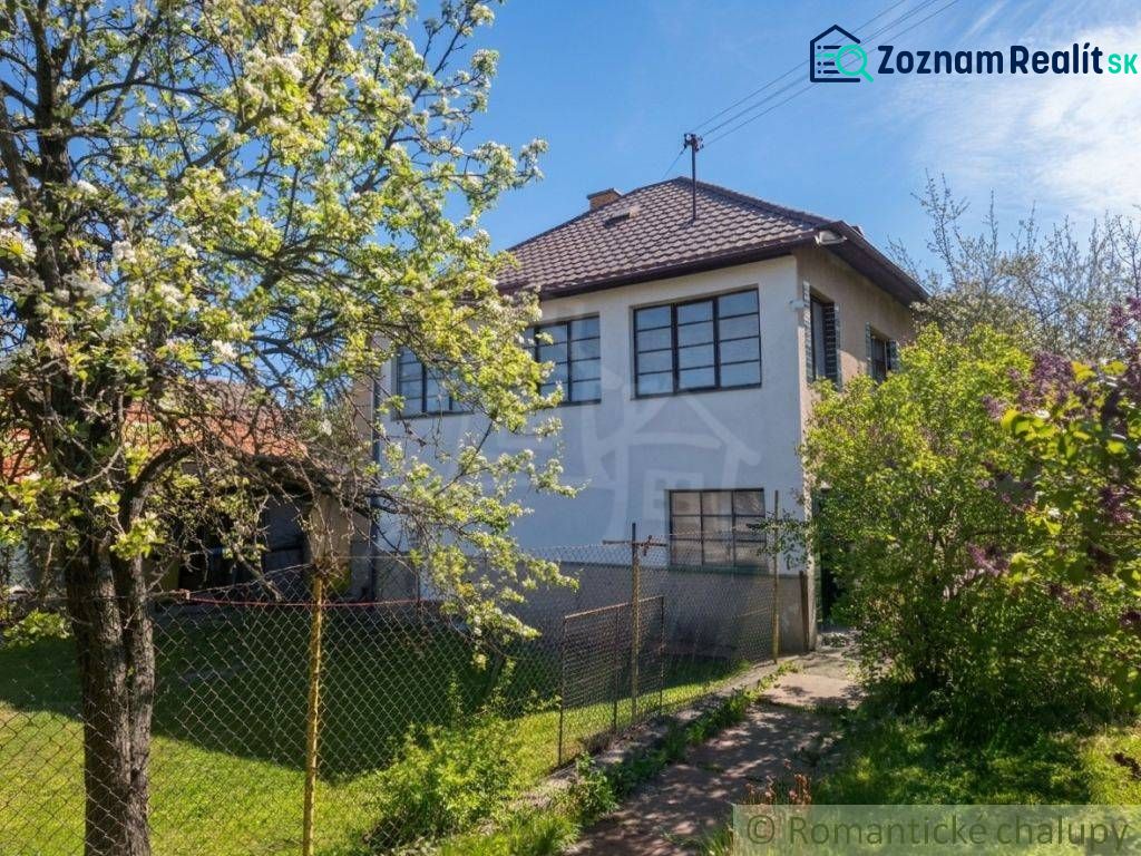 A family house in Kriváň with a front garden, a blooming tree, and a blue sky.