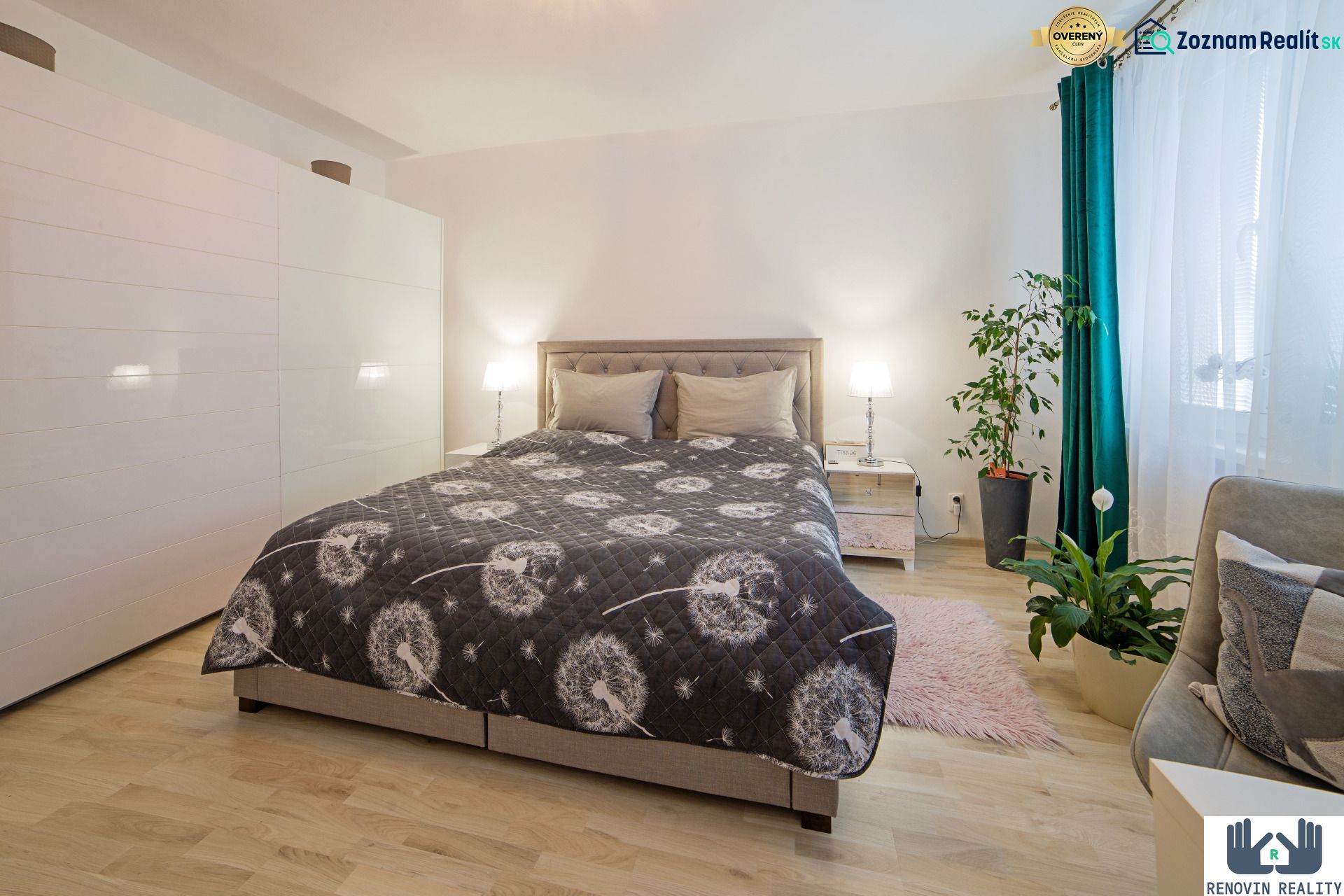 A bright bedroom with a large bed, wardrobes, and plants in a studio apartment, with a wooden decor floor.