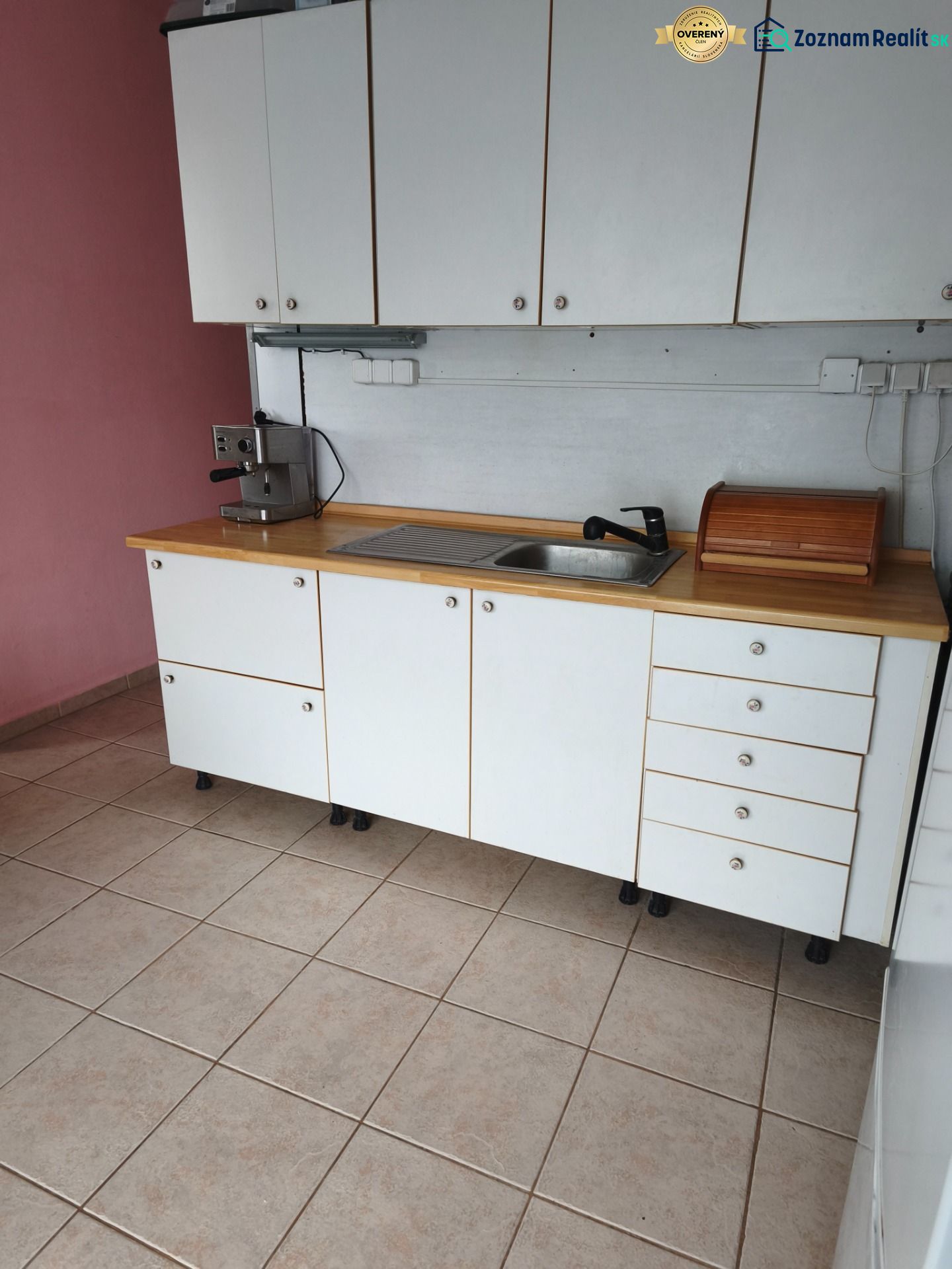 A kitchen in a 2-room apartment with white cabinets, tiles, and a coffee maker.