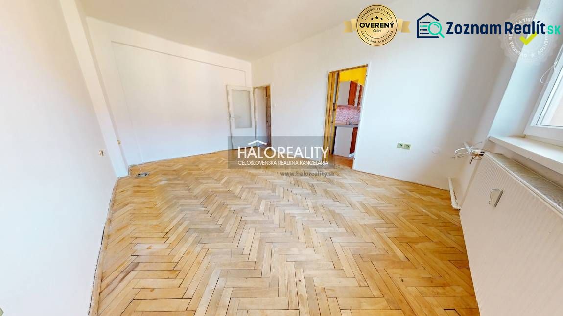 A room in a 2-room apartment with a large floor with wooden decor, white walls, and a window.
