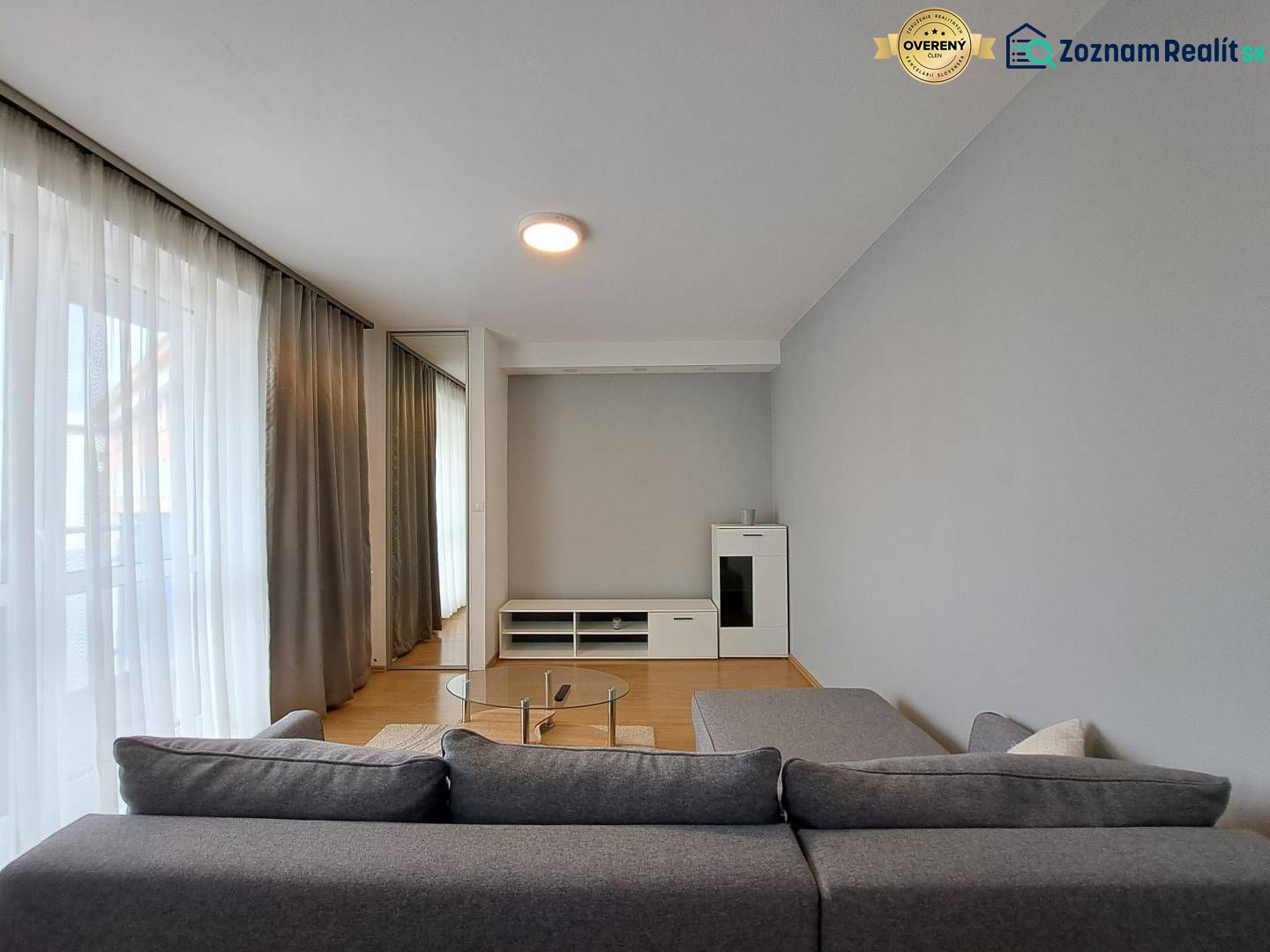Living room in a three-room apartment with a sofa, glass table, and wooden decor flooring.