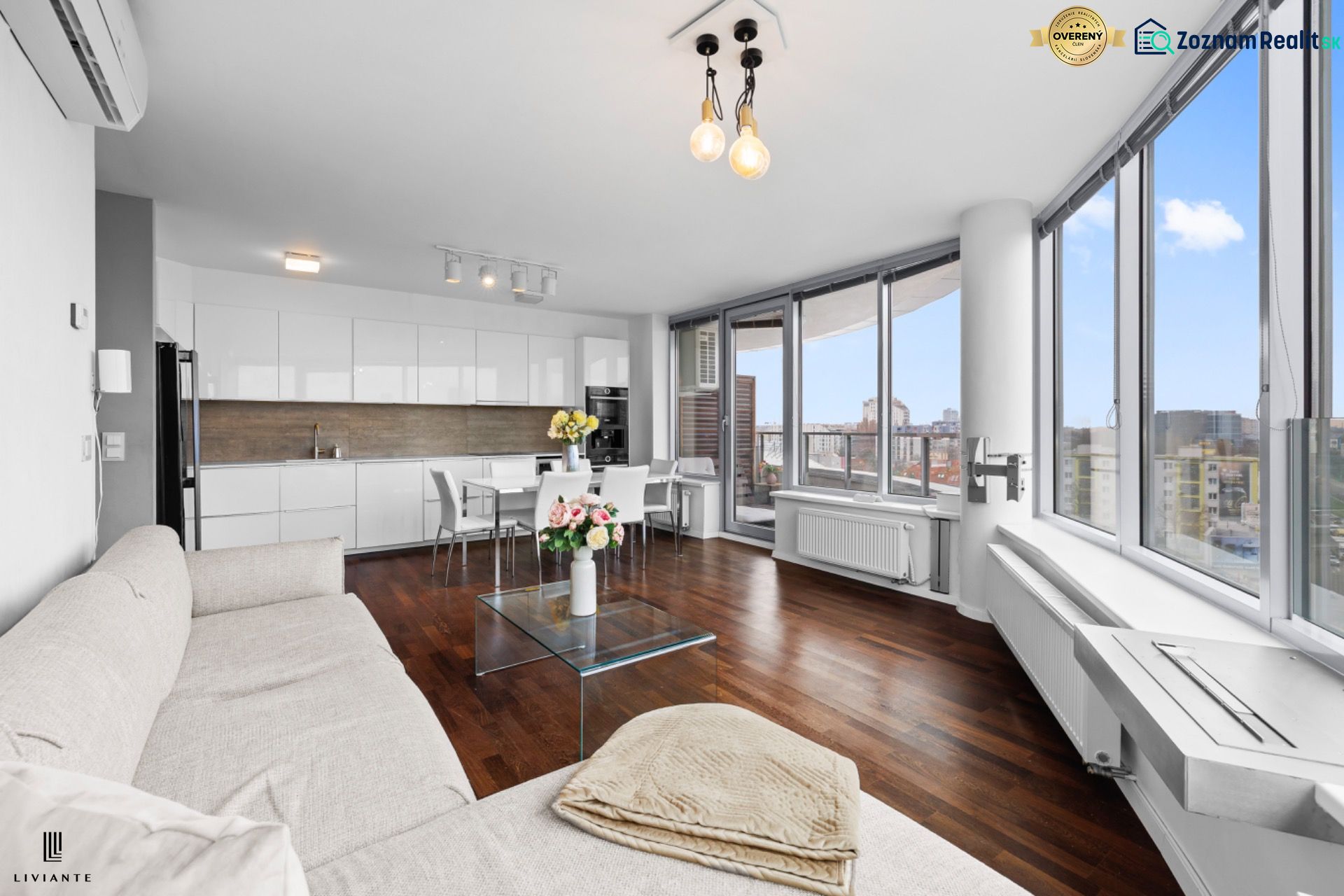 Living room and kitchen in a 3-room apartment with a wooden decor floor, large windows, and a sofa.