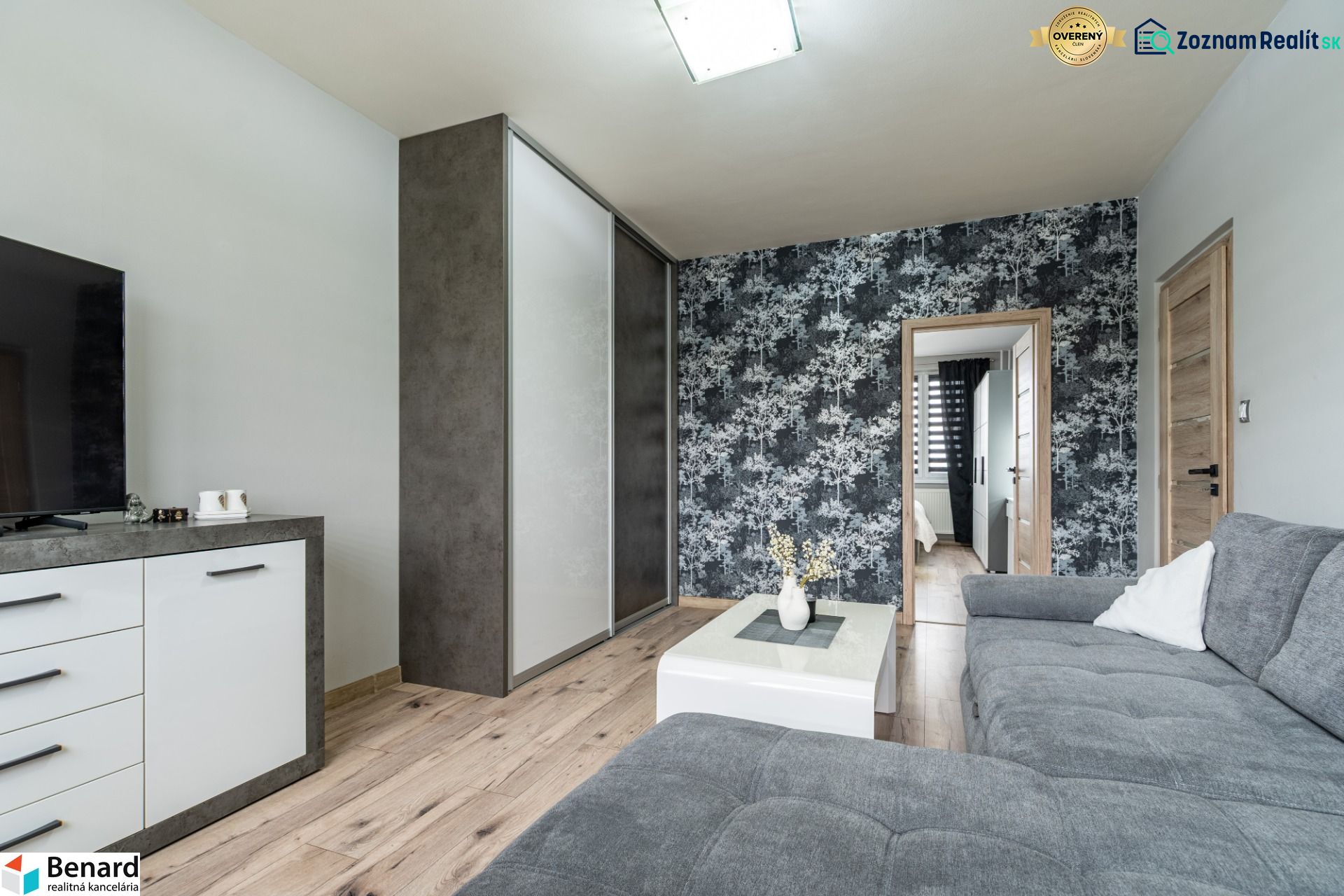Living room with a sofa, cabinet, wallpaper, and wooden decor flooring in a 2-room apartment.