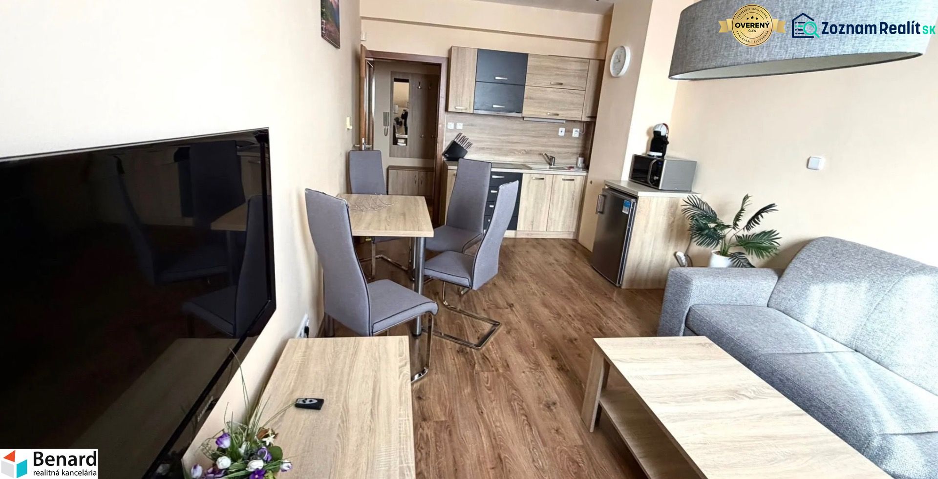 Living room of a two-room apartment with a kitchen, sofa, and wooden decor flooring.
