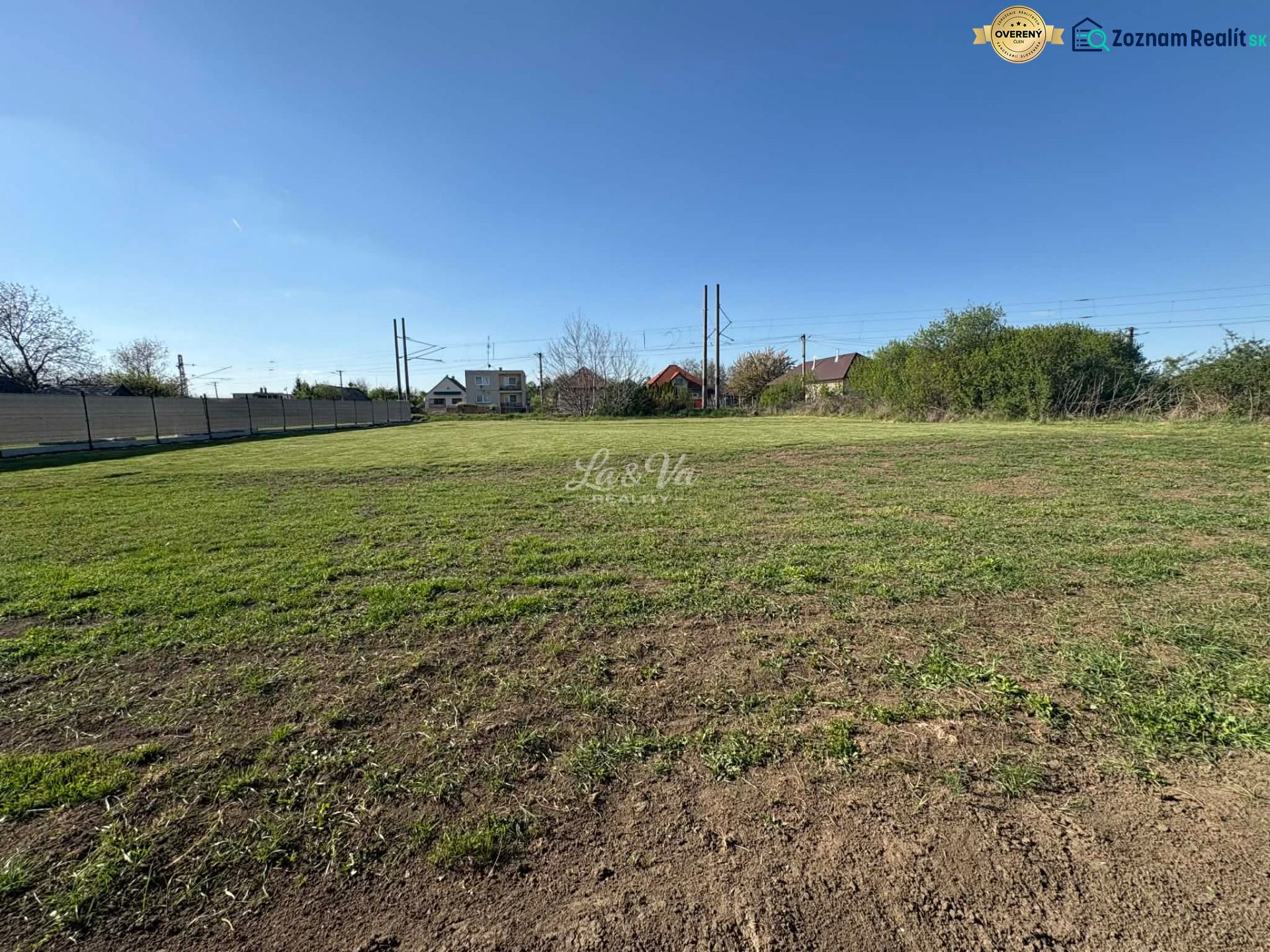 A flat plot of land in Pozba designated for residential use, with a view of neighboring houses.