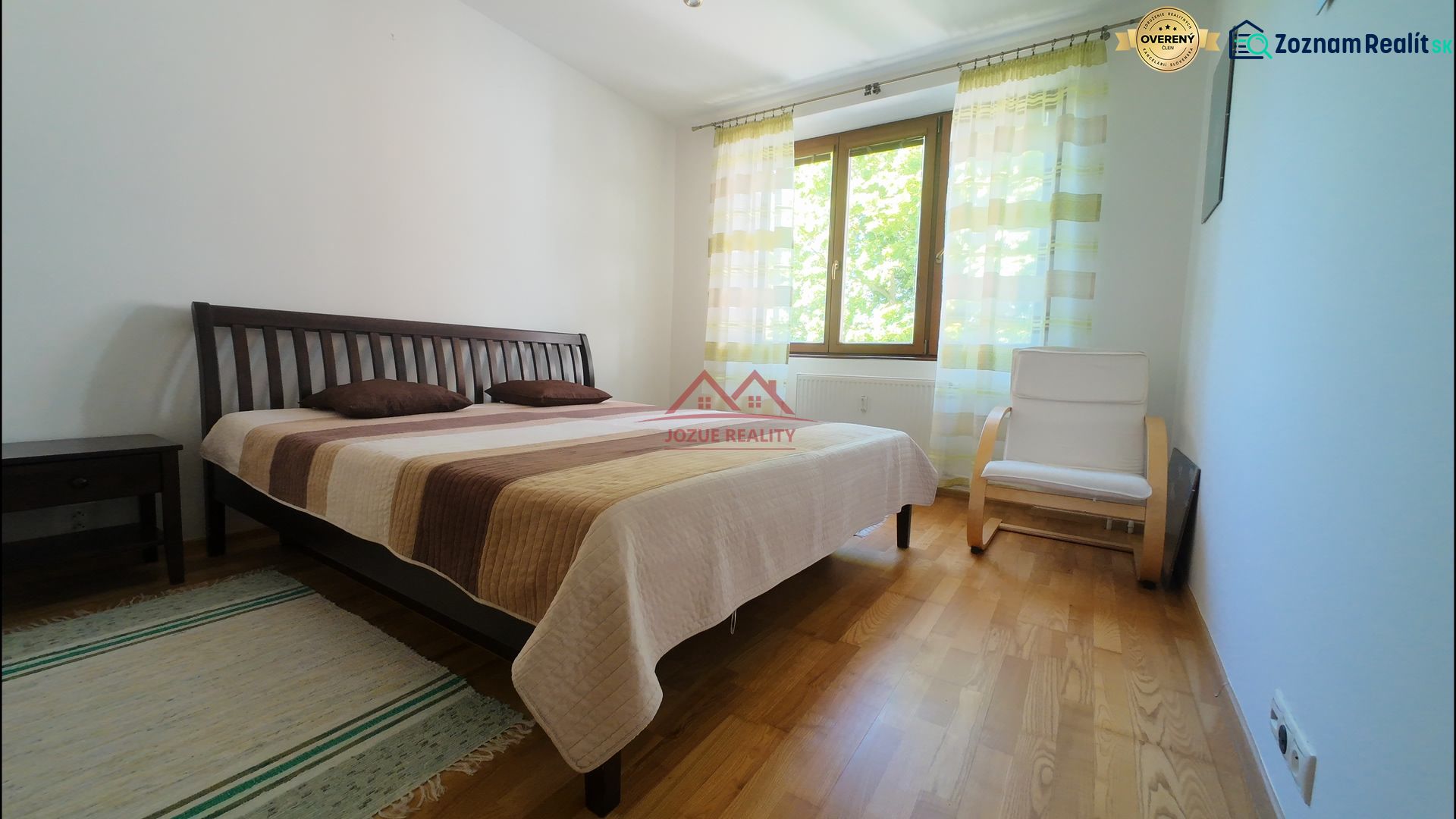 Bedroom in a 2-room apartment with wood-patterned flooring, a bed, and a chair.