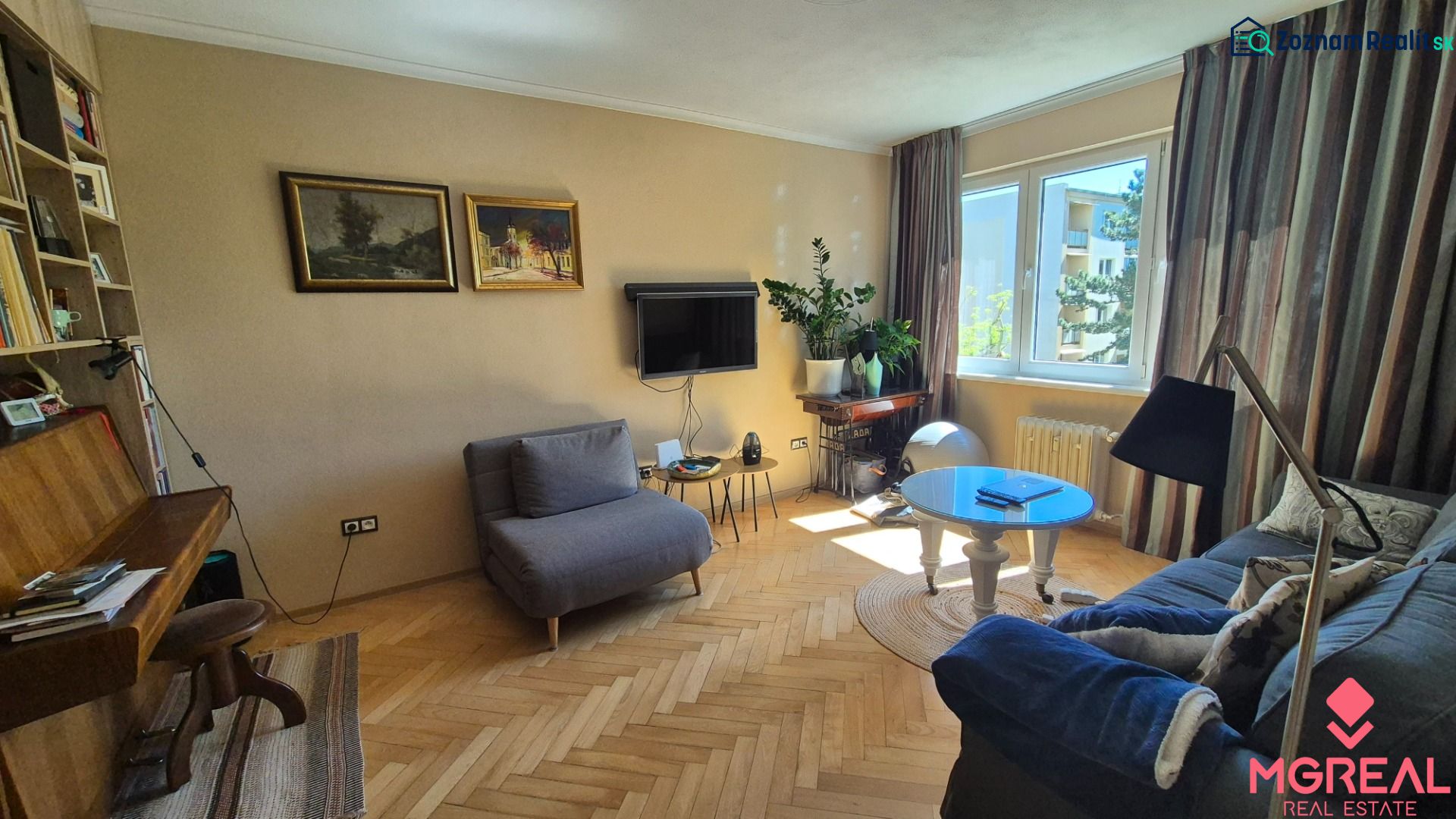Living room in a 2-room apartment with a wooden decor floor, a sofa, and a television.