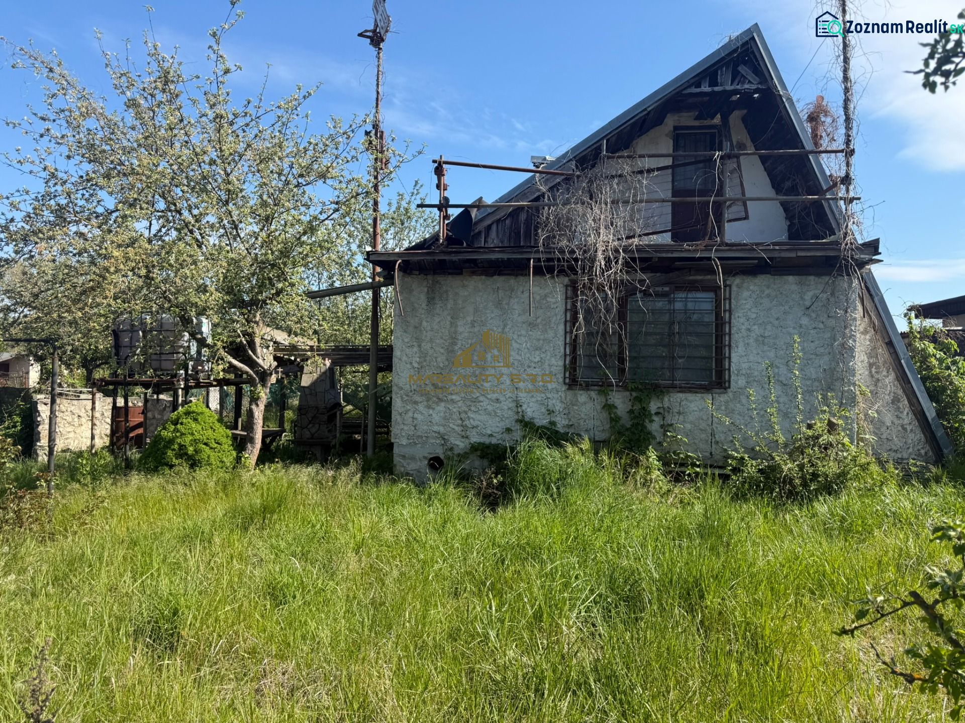 A cottage in Malacky with an overgrown garden, trees, and a neglected facade.