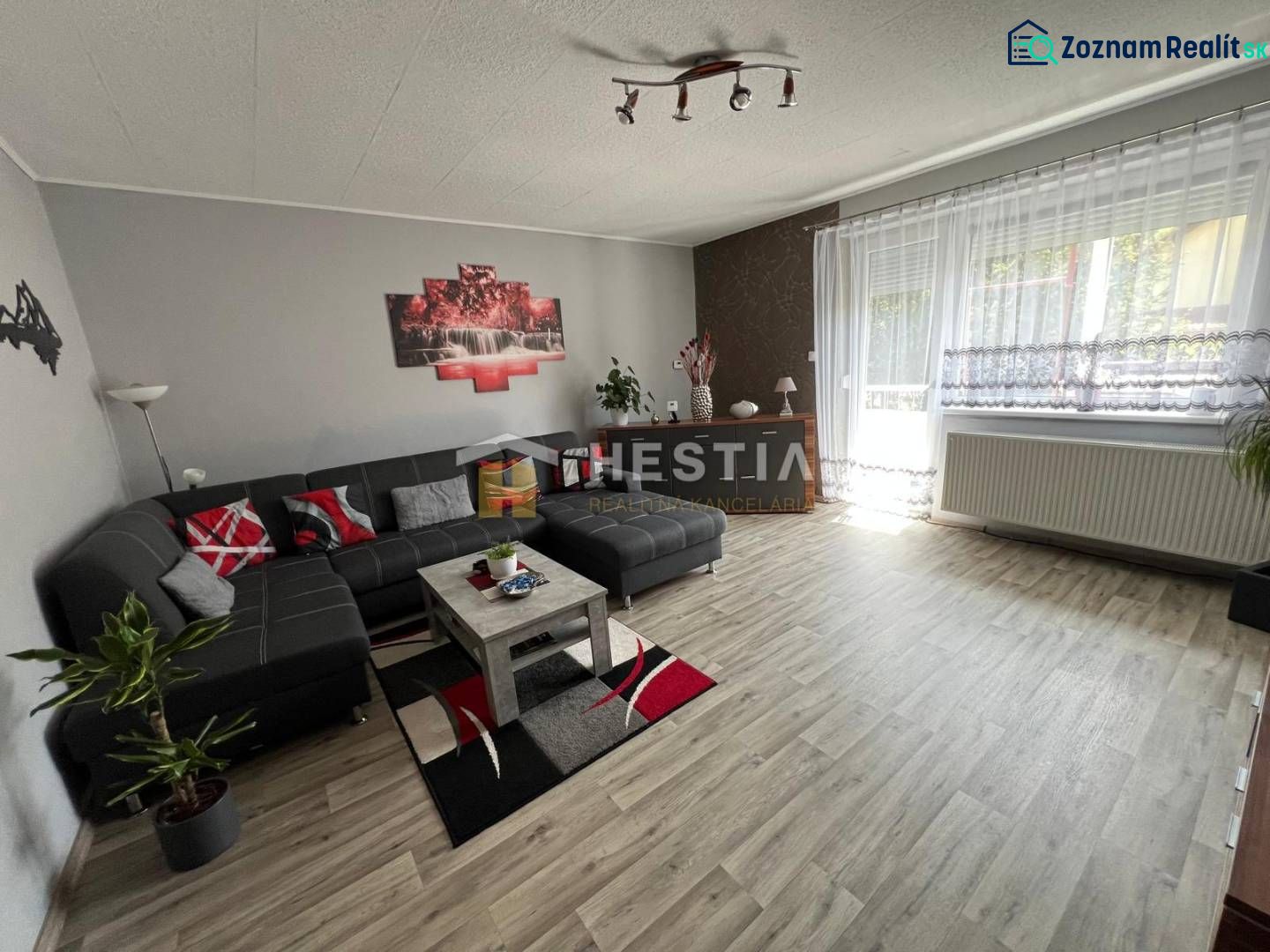 A spacious living room in a three-room apartment with a wooden decor floor and a comfortable sofa set.