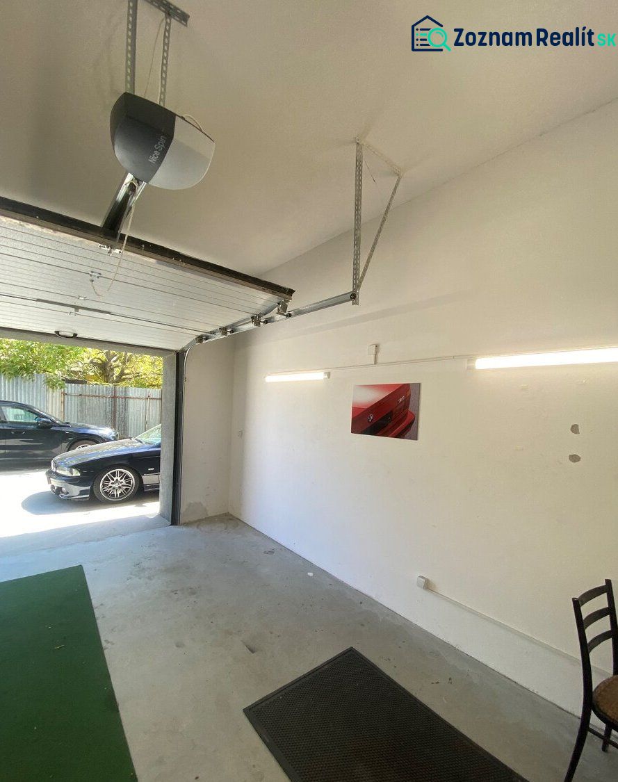 A garage with open doors, a car outside, a bright interior, a picture on the wall.