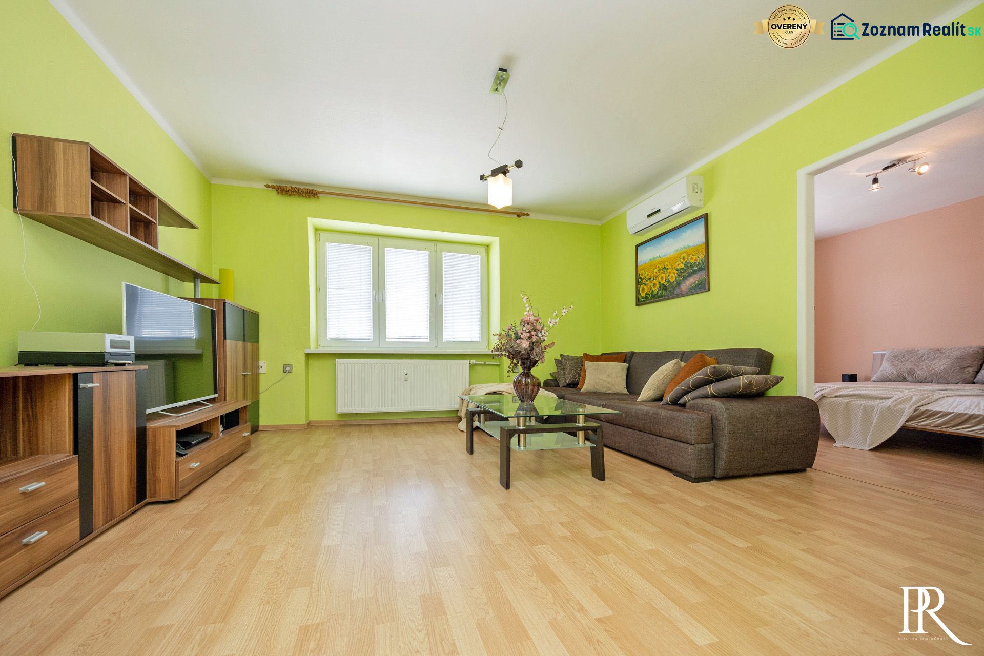 A living room with a wood-patterned floor, a sofa, and a painting in a two-room apartment.
