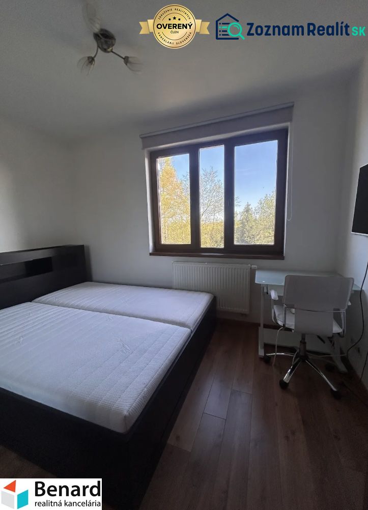 A bedroom with a bed, table, and wooden decor flooring in a three-room apartment.