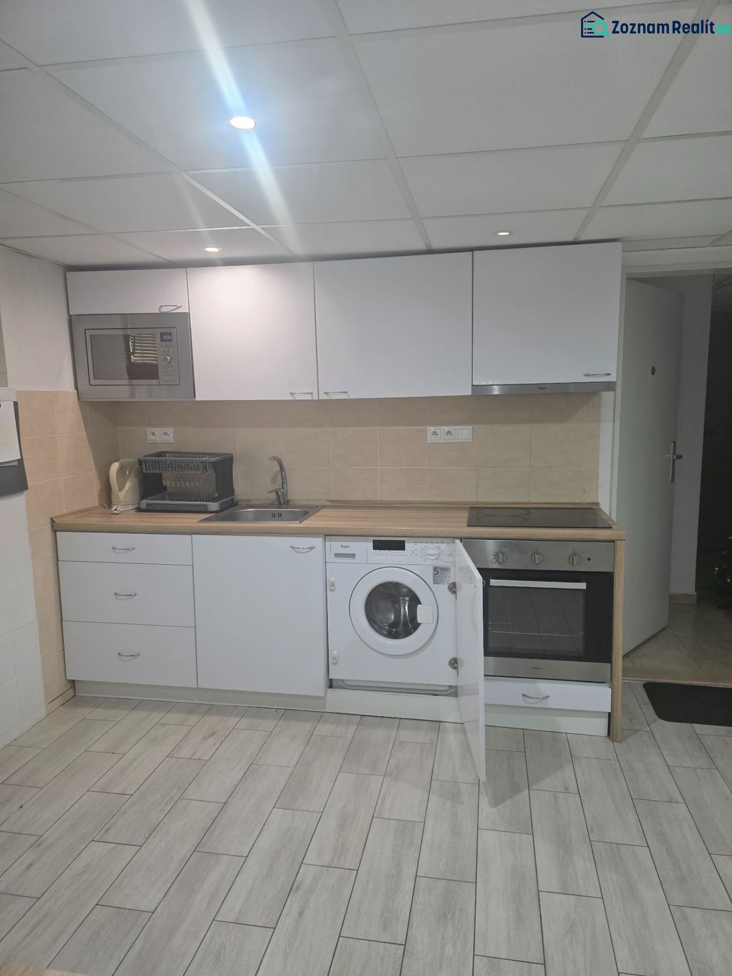 A kitchen in a one-room apartment with white kitchen cabinets and a wooden decor floor.
