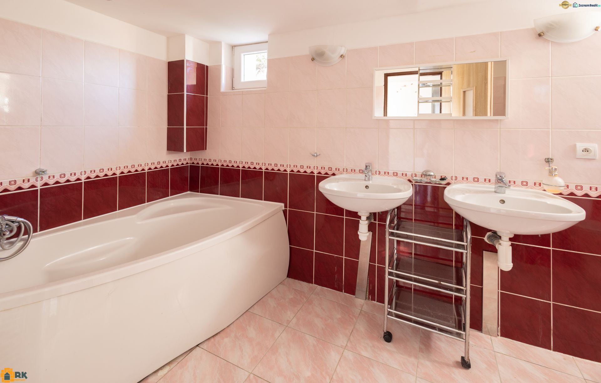 A bathroom in a family house with a corner bathtub and two sinks on pink-red tiles.