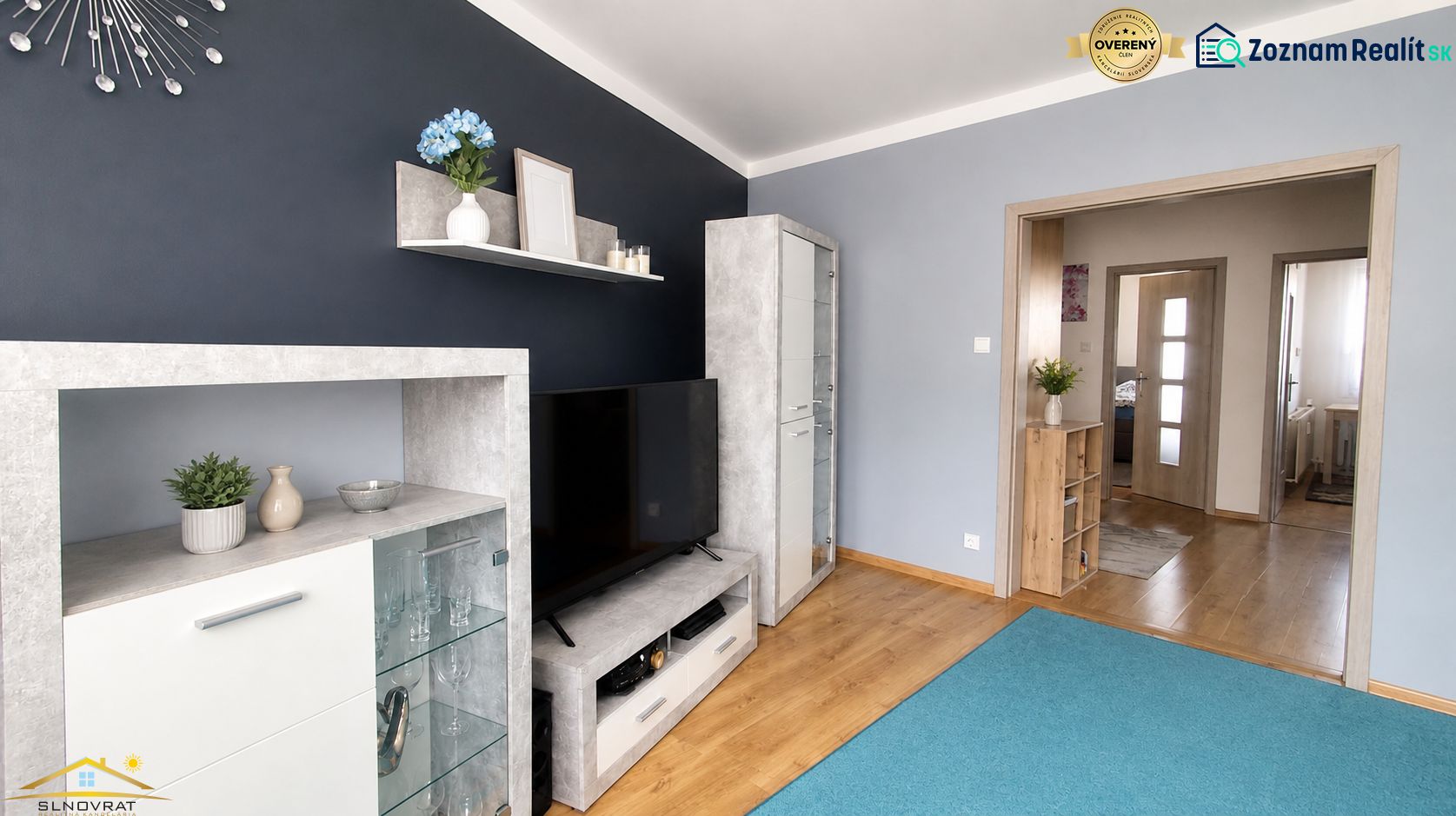 Living room in a 3-room apartment with shelves, a television, and a wooden decor floor.