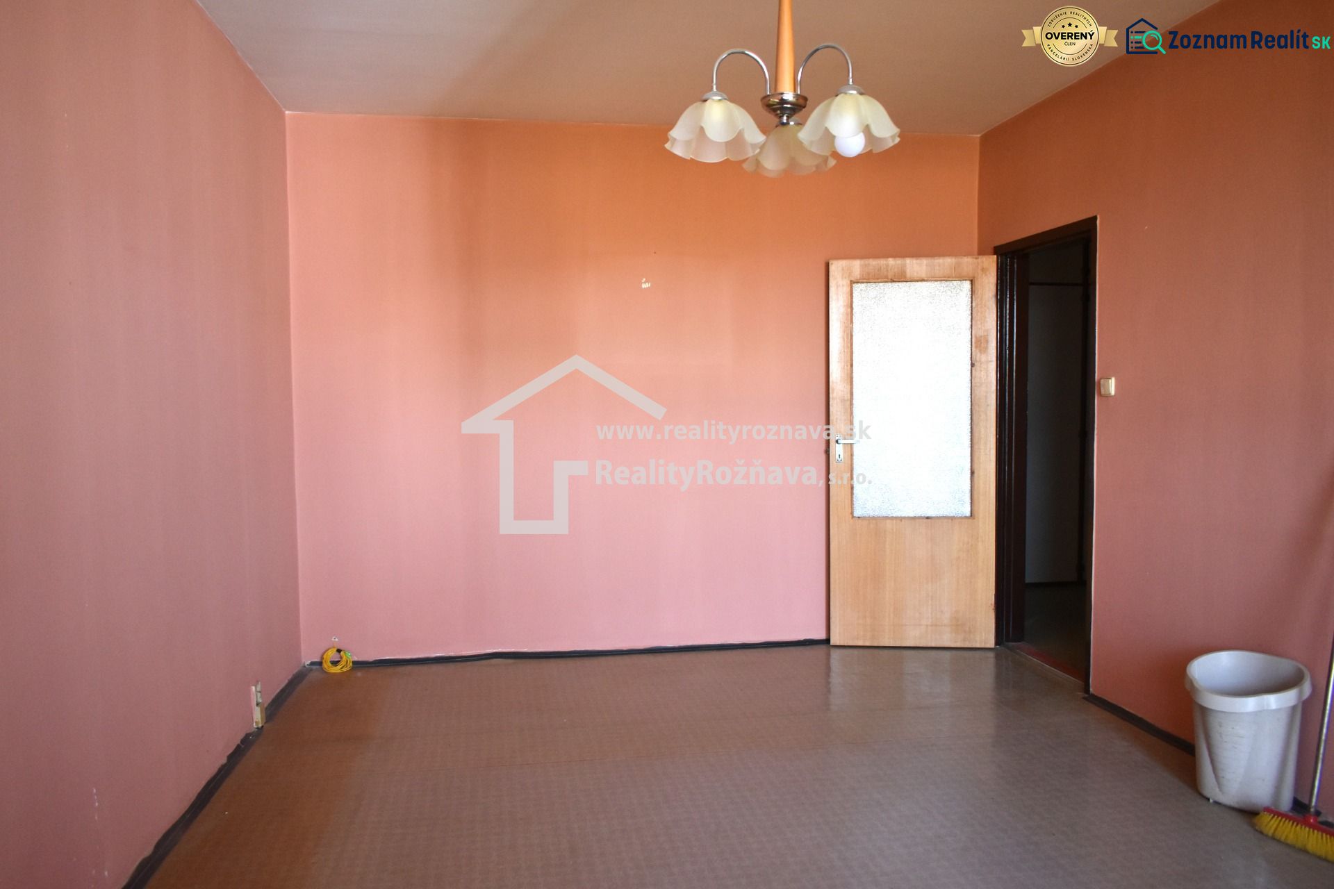 A room with pink walls and a brown floor in a 3-room apartment.